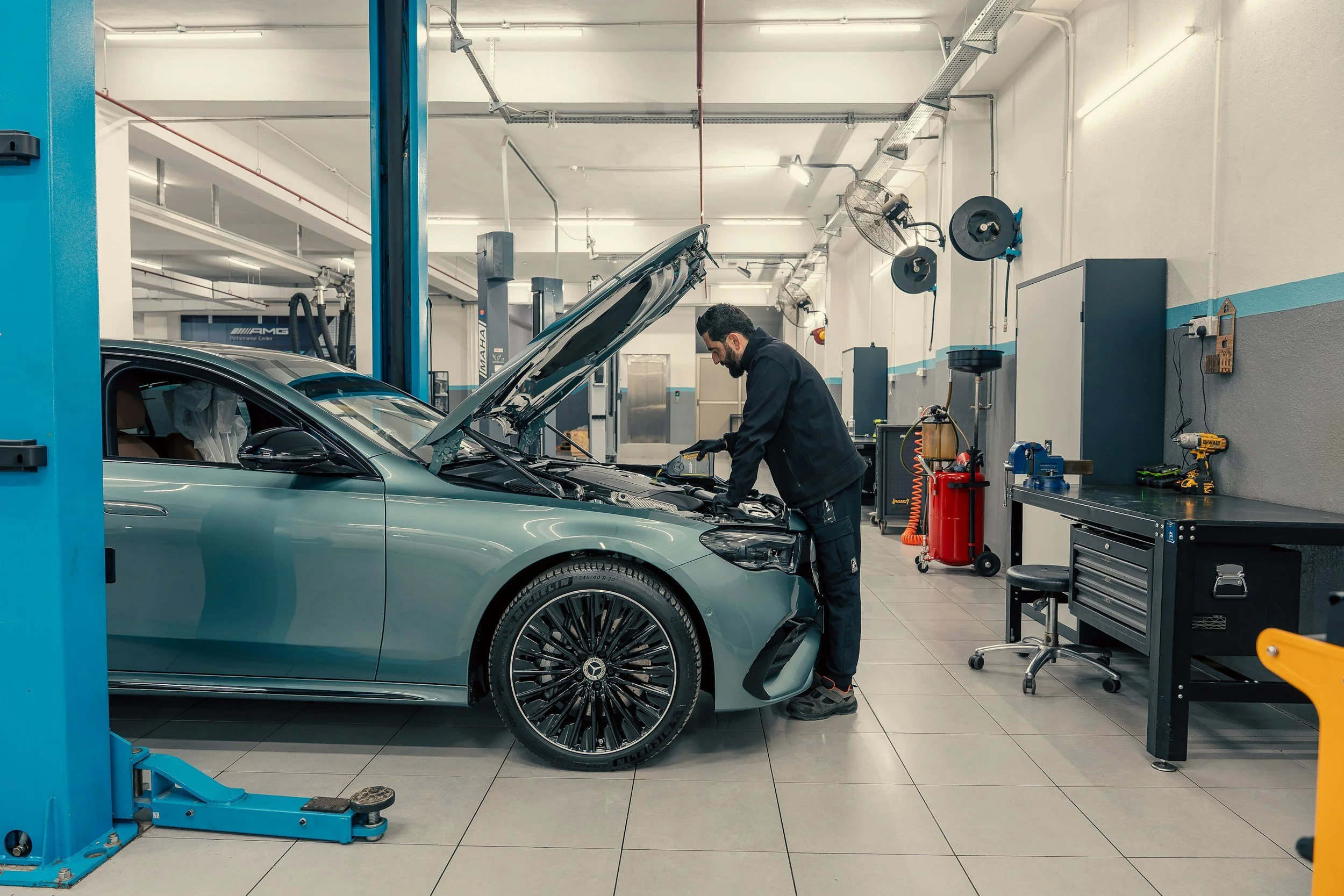 Hombre revisando un automóvil en un taller mecánico, con herramientas y equipos de reparación alrededor.