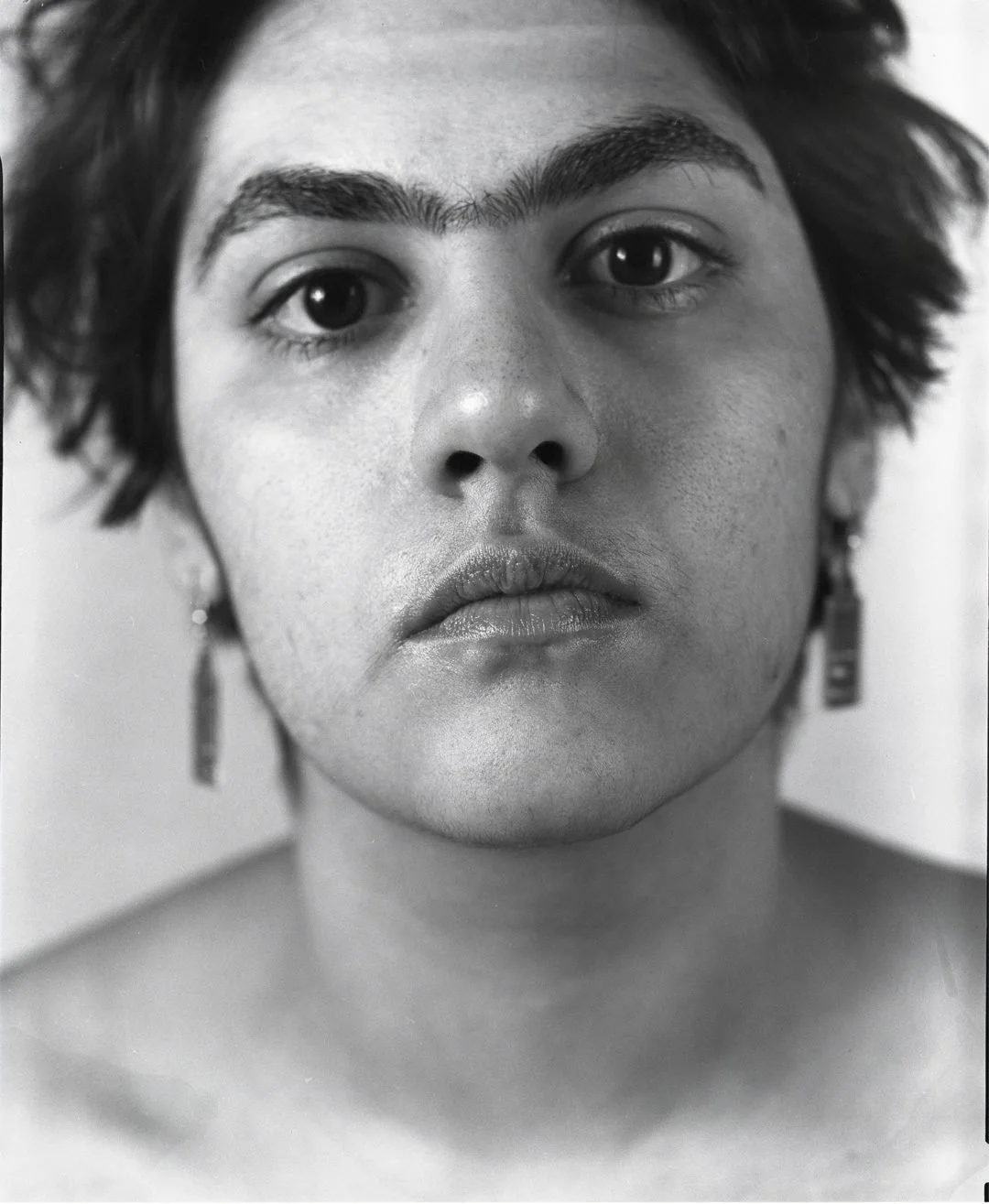 Close-up black-and-white portrait of a woman with short, dark hair, wearing earrings, looking directly into the camera.