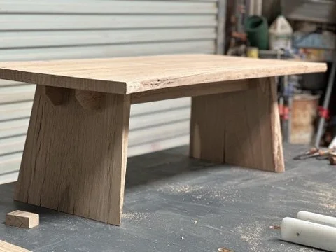 Unfinished wooden table or bench in a workshop with tools and supplies in the background.