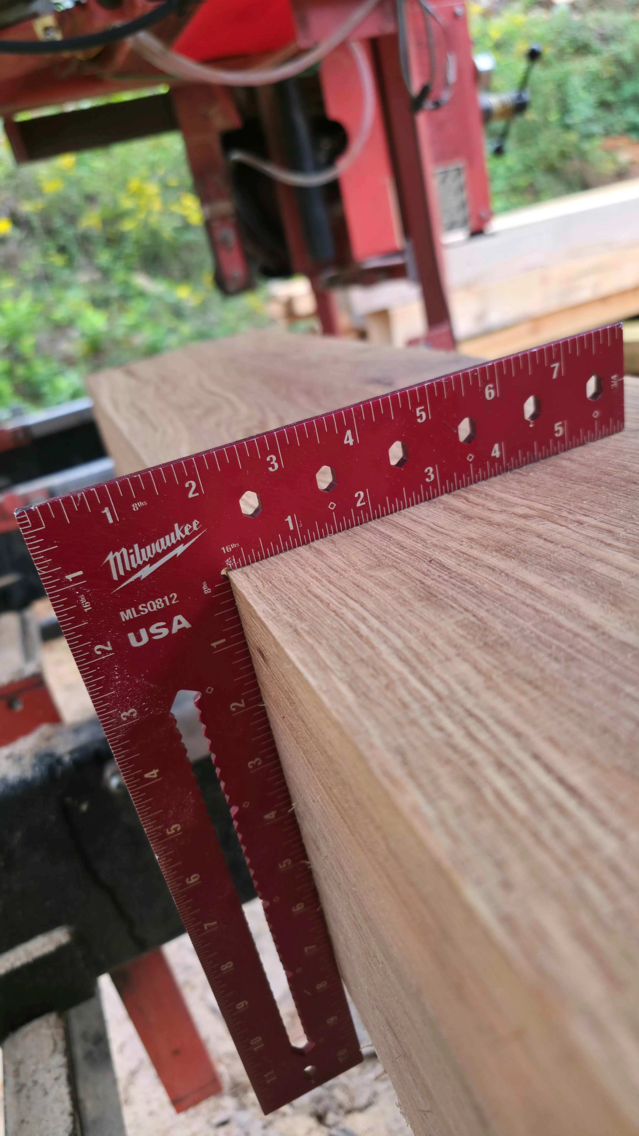 Close-up of a red Milwaukee speed square placed on a rectangular piece of wood being measured at 8 inches.
