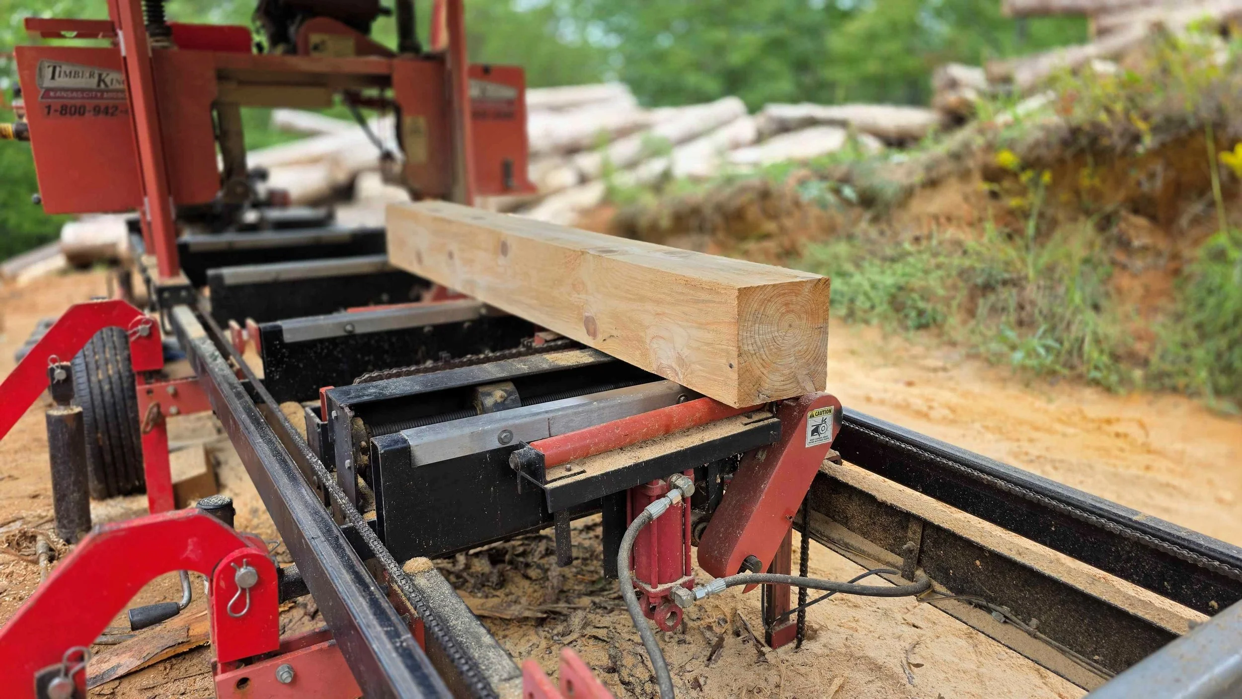 A pine beam is on a red sawmill outside.