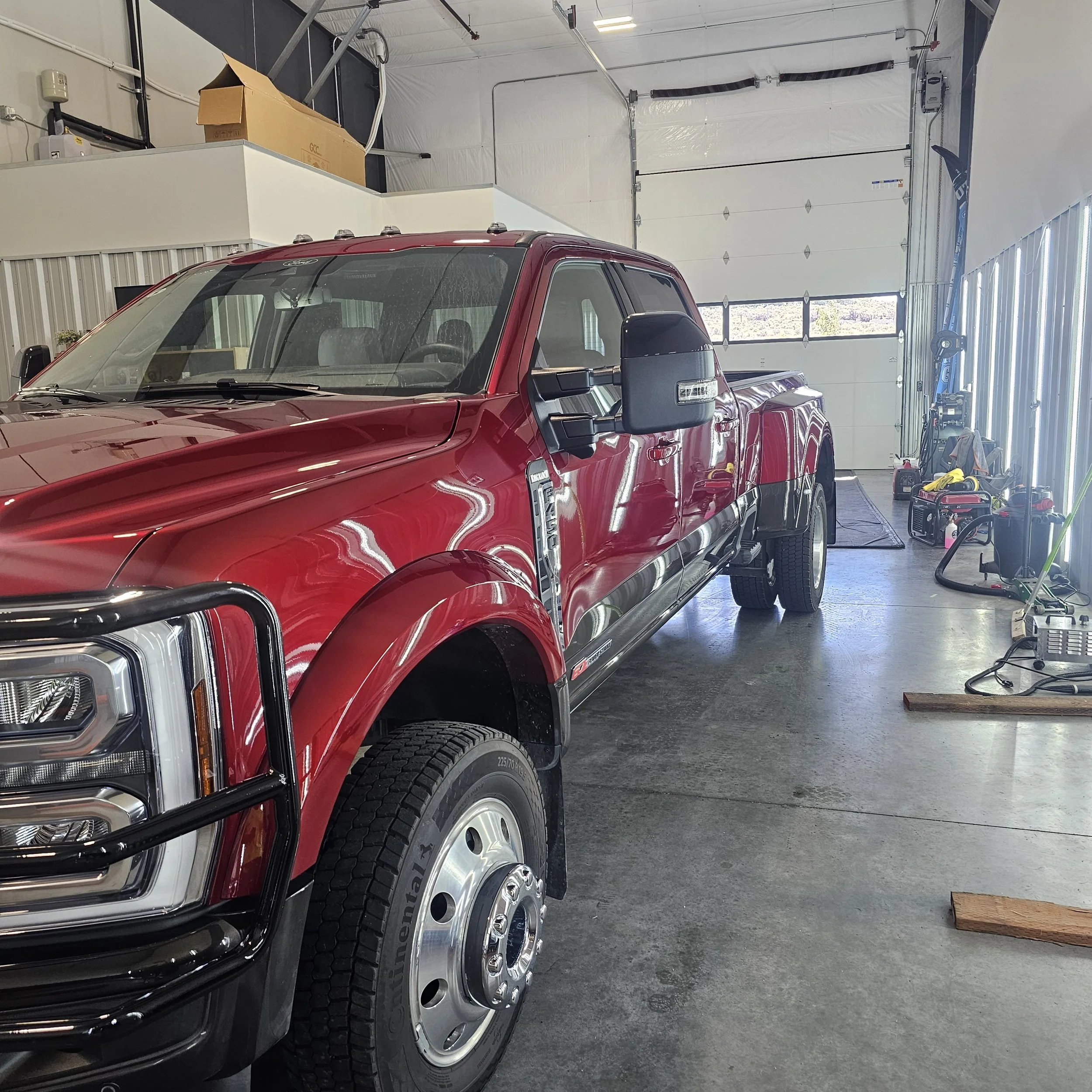 Red pickup truck parked inside a garage with a white door, next to various tools and equipment.