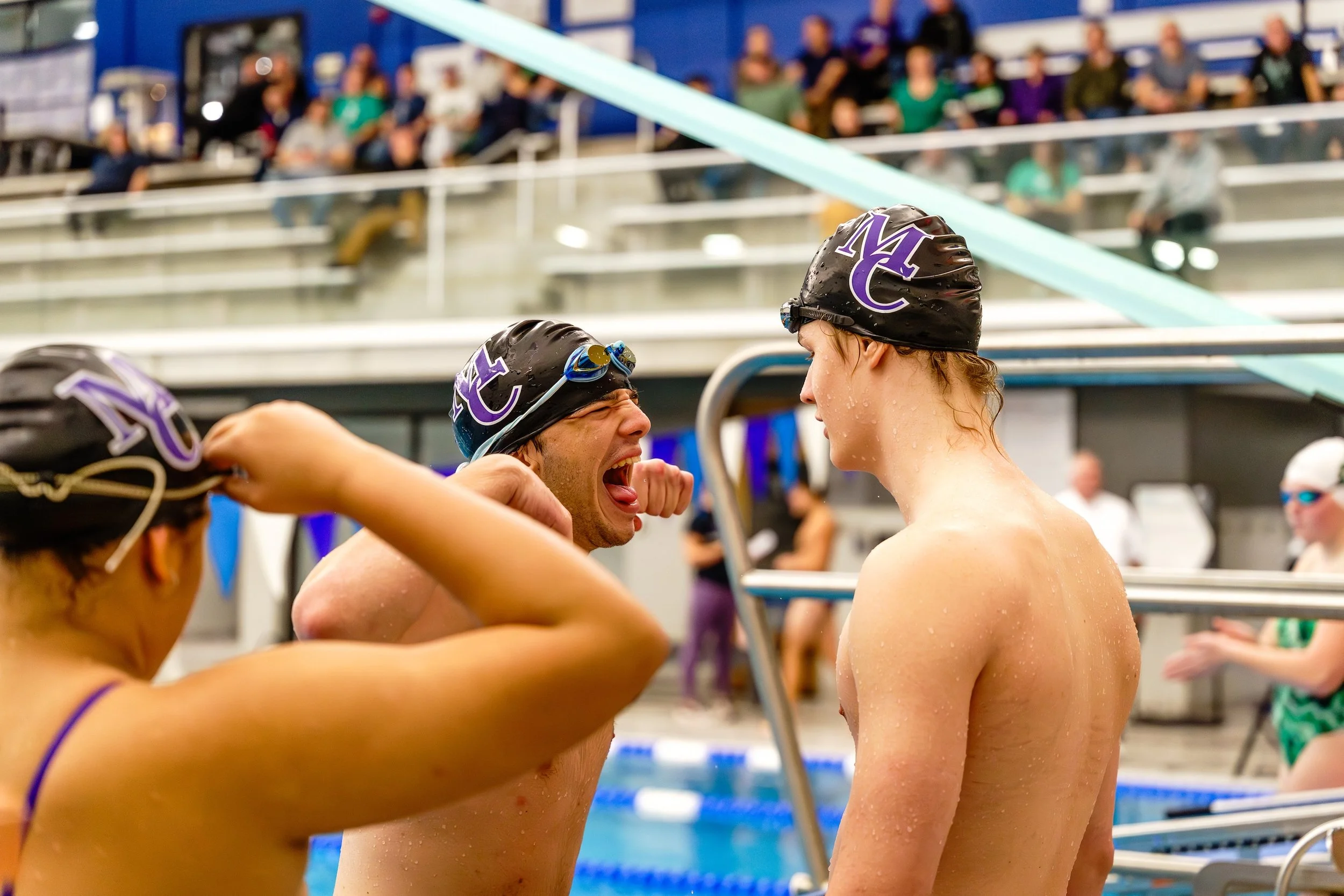 Two male swimmers with swim caps and goggles talking after a race at an indoor swimming pool event.