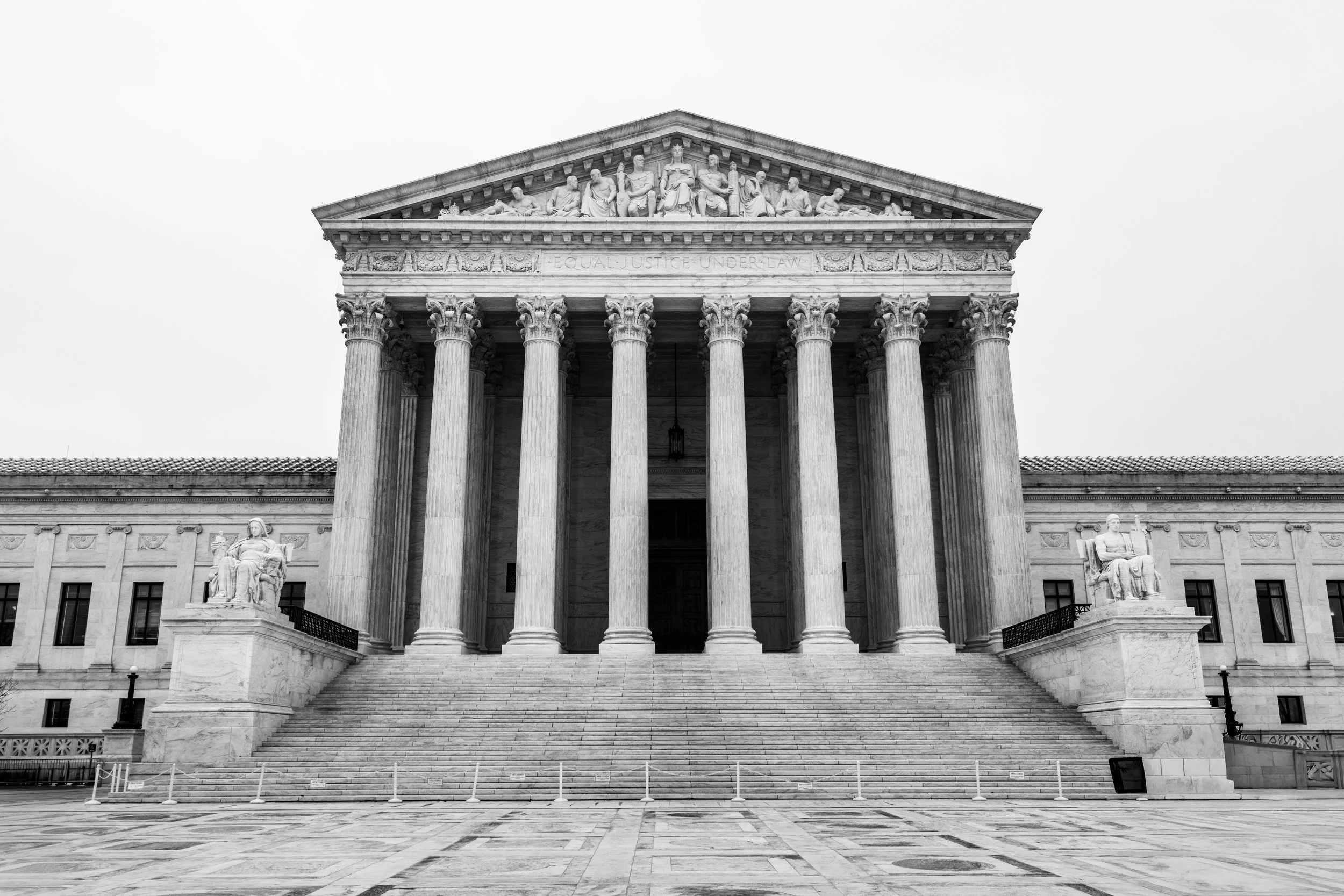 The United States Supreme Court building with classical architecture, tall columns, and statues, viewed from the front with steps leading up to the entrance in black and white.