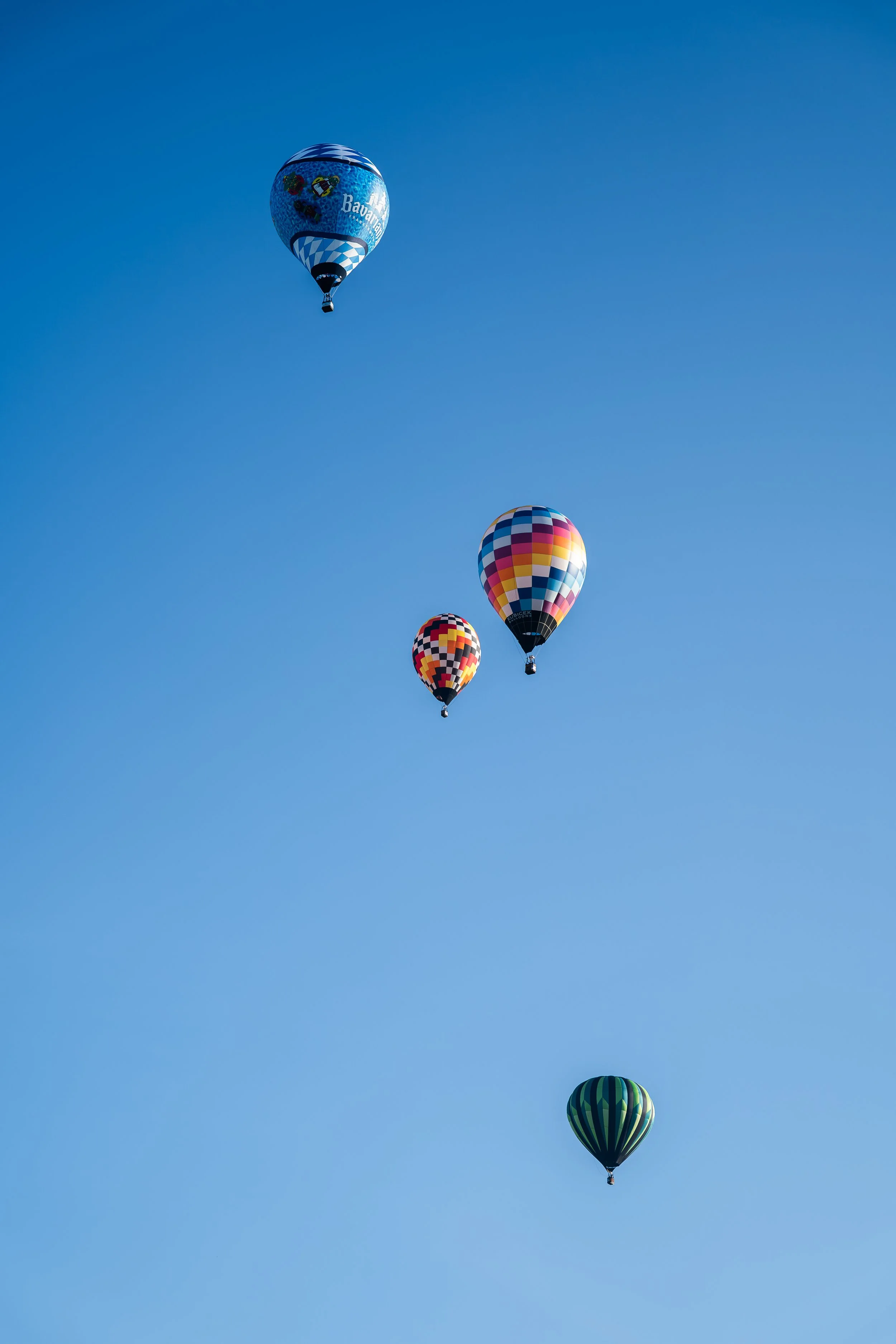 Five colorful hot air balloons flying in a clear blue sky.