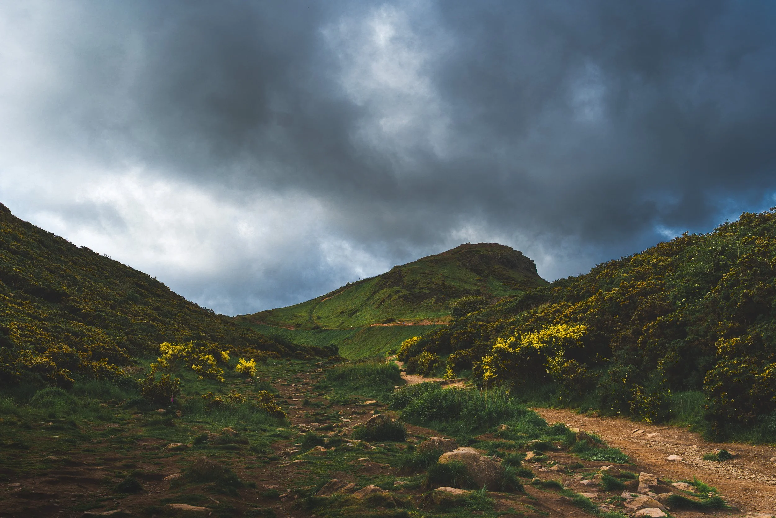 Scenic view of green hills with a dirt path and cloudy sky.