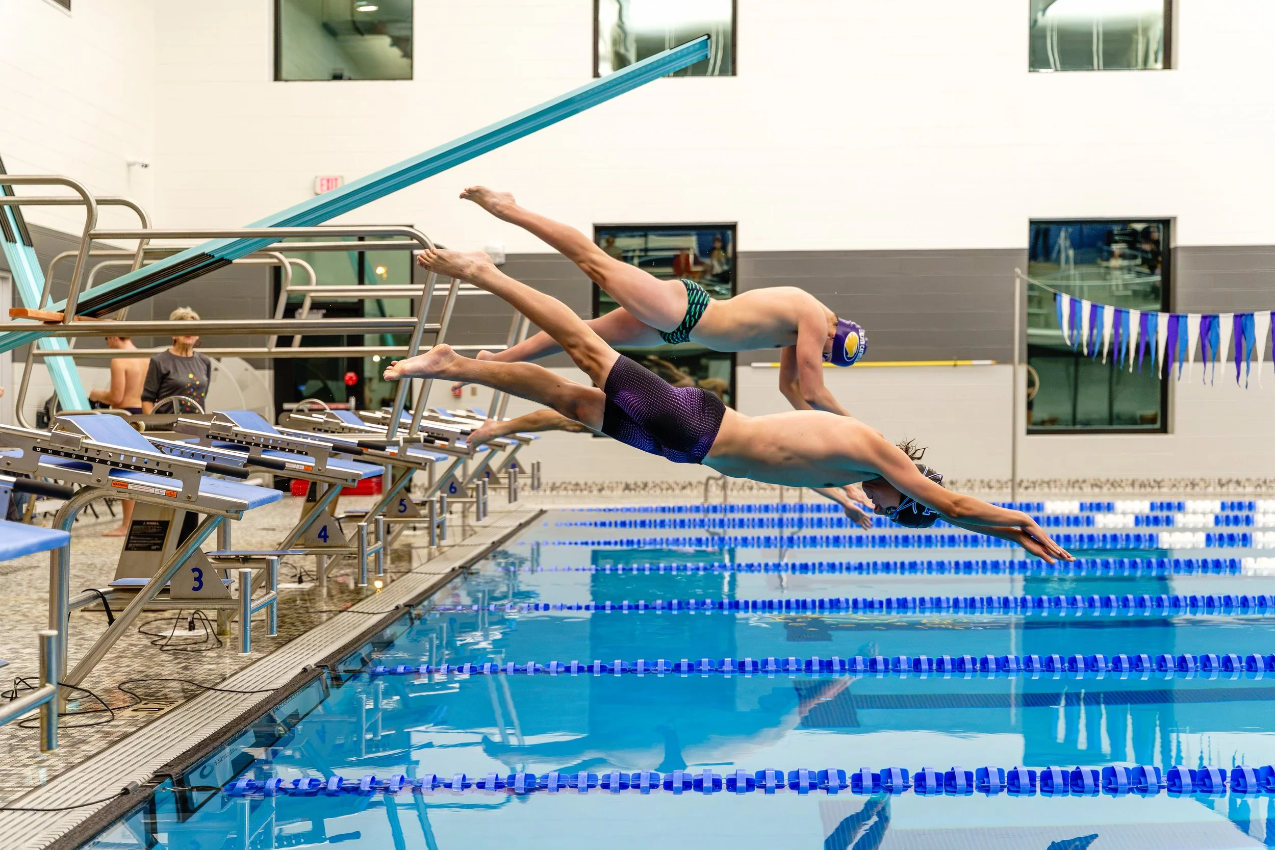 Swimmers dive into an indoor swimming pool from starting blocks.
