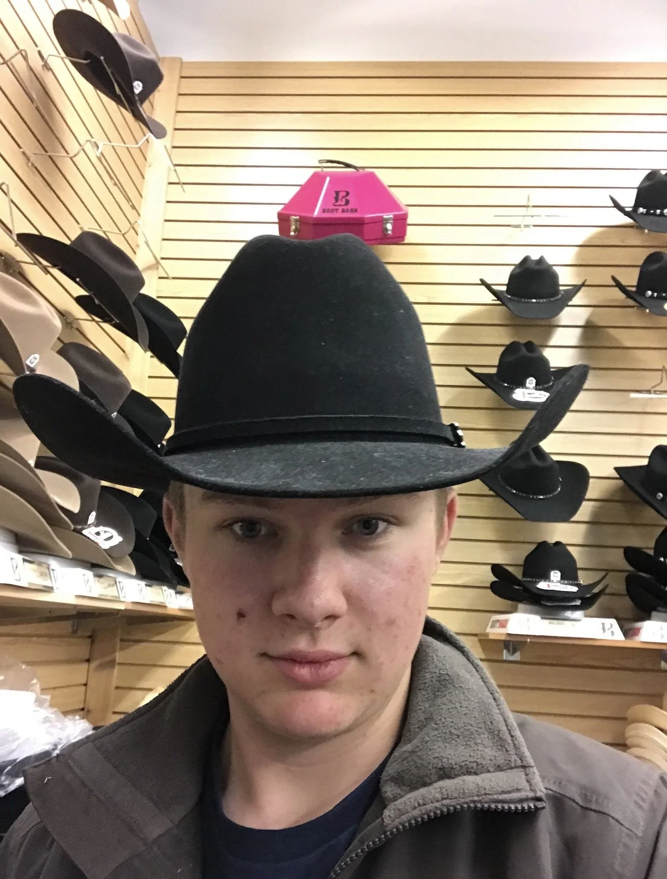 Person trying on a black cowboy hat in a store with display shelves filled with hats on the walls.