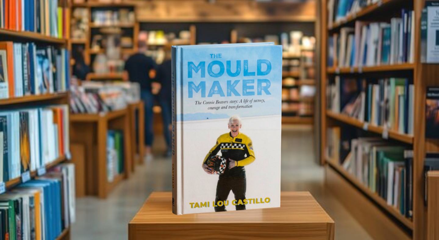 Book "The Mould Maker" on a wooden pedestal in a library or bookstore setting.