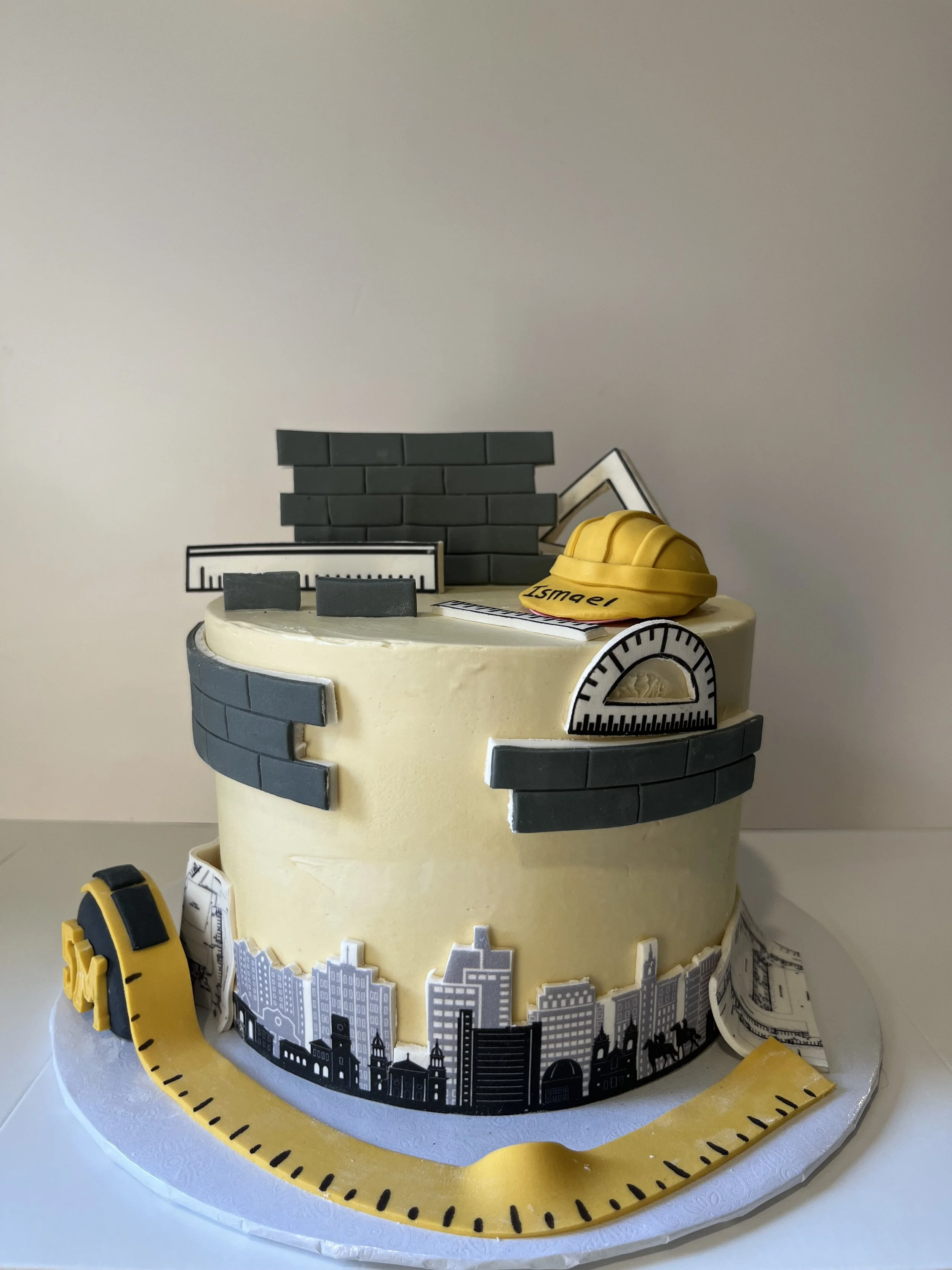 A decorative cake featuring a cityscape, construction safety helmet, and tools, representing urban development or construction theme.