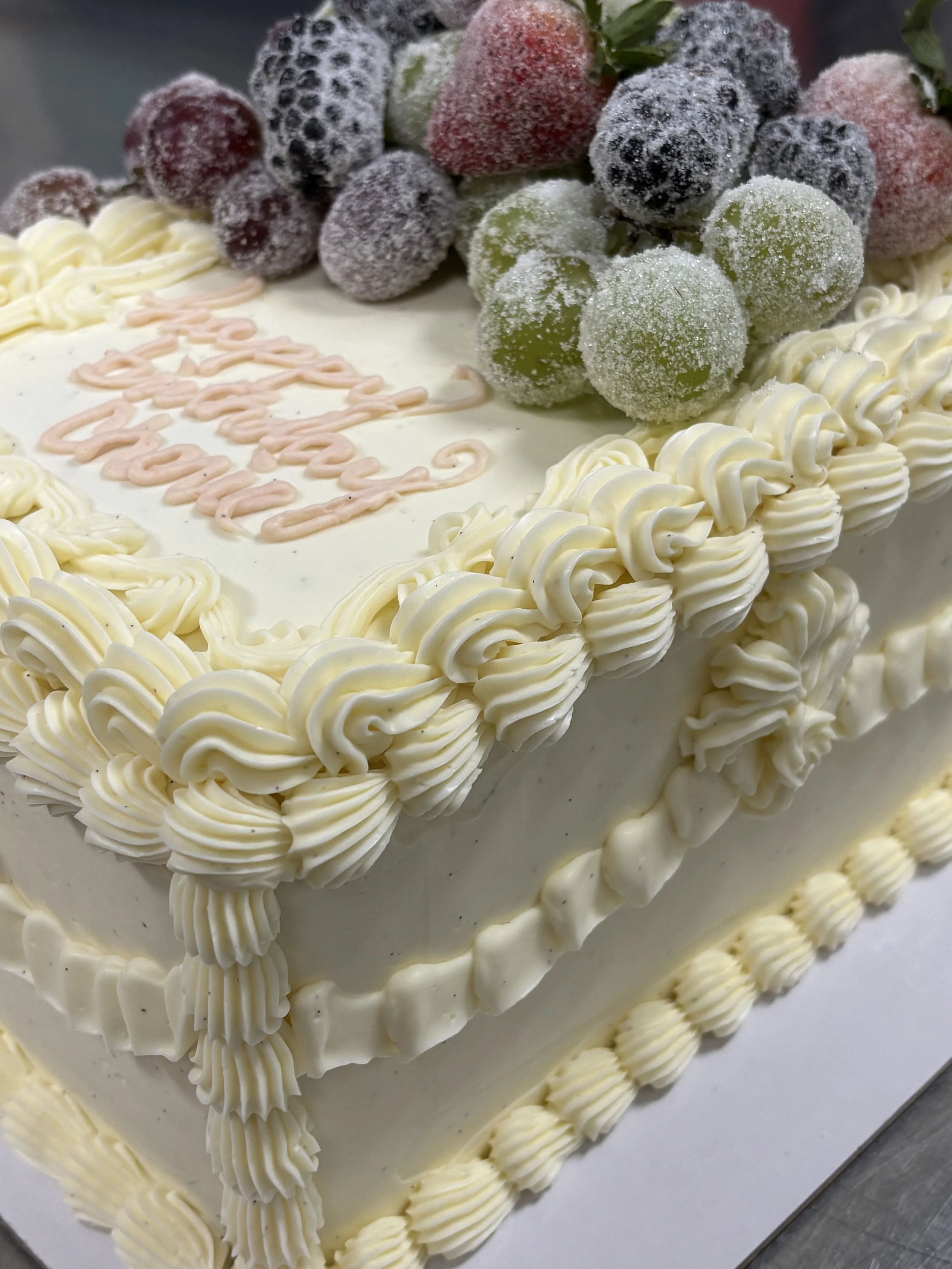 Close-up of a white frosted birthday cake decorated with berries and white piping.