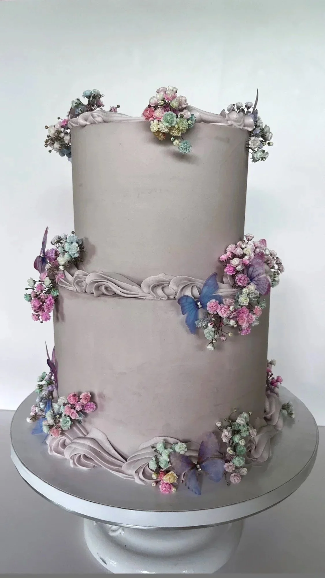 A multi-tiered cake decorated with pastel-colored flowers and blue butterflies.