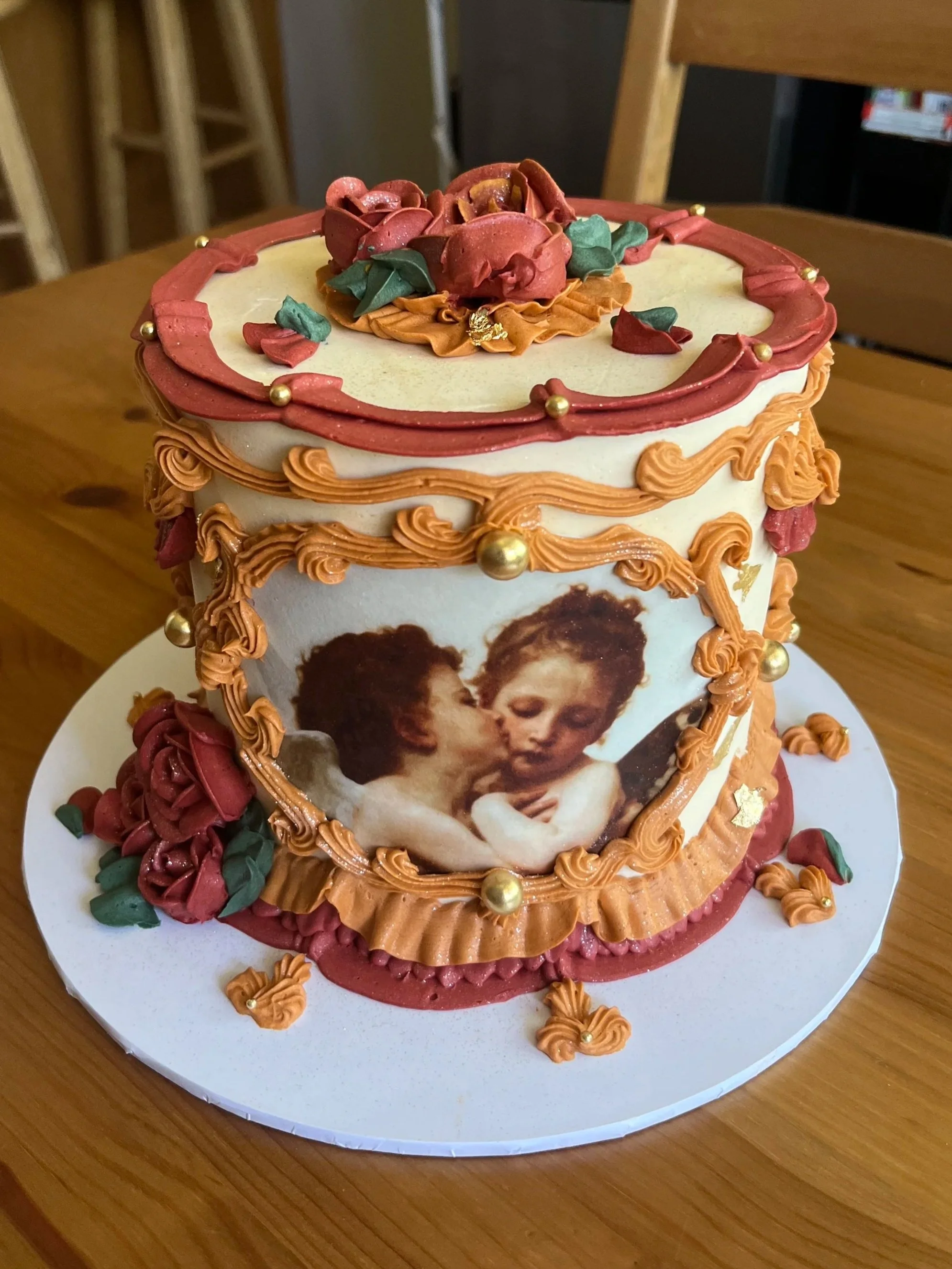 A cake decorated with an image of two children kissing, surrounded by pink and orange frosting with gold and green decorative elements.