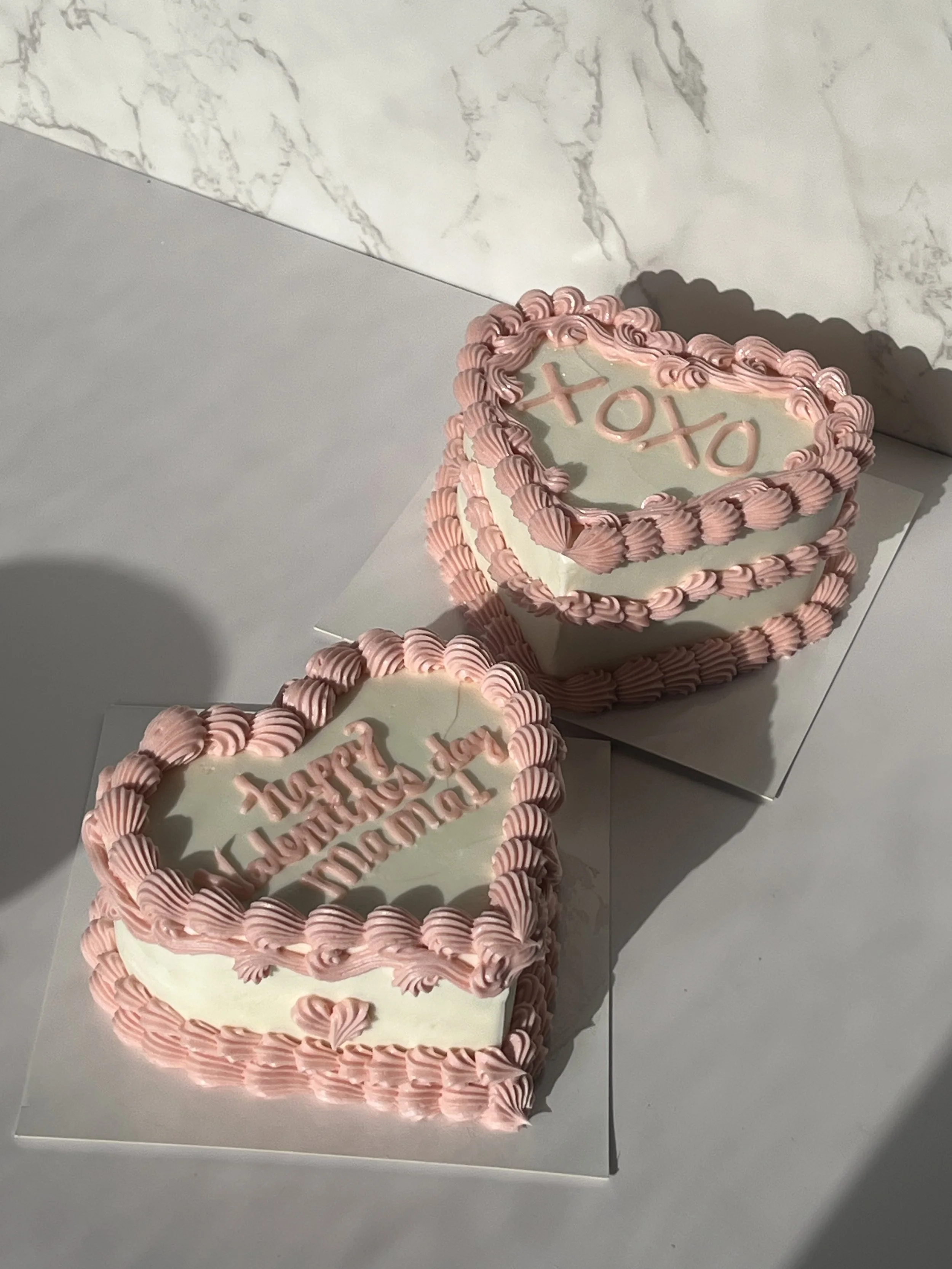 A birthday cake with pink frosting in heart shapes and the message 'XOXO' on top, along with several matching cards or decorations.