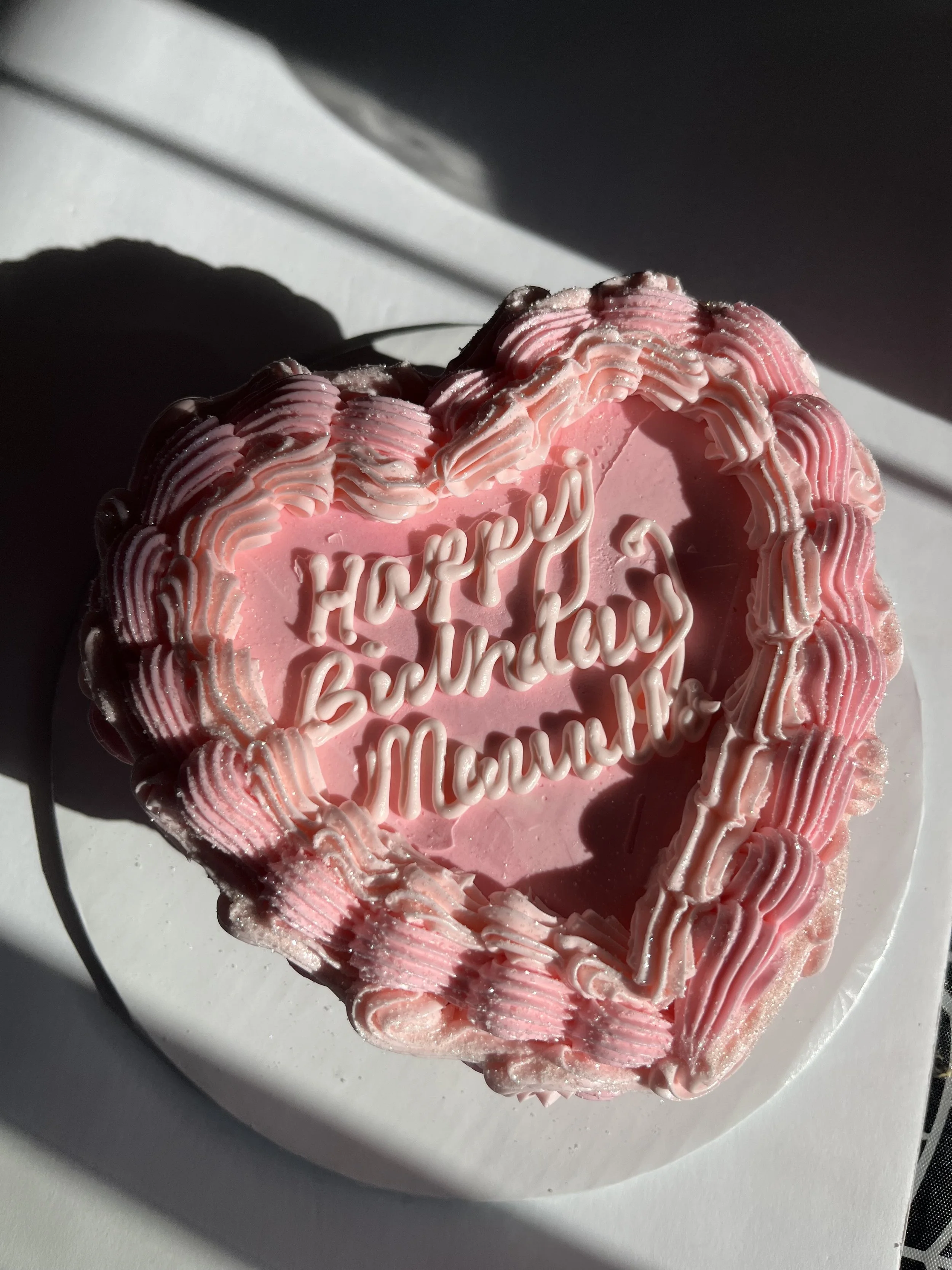 Heart-shaped cake with pink icing and white piped decorations, with a message that says 'Happy Birthday' on top.