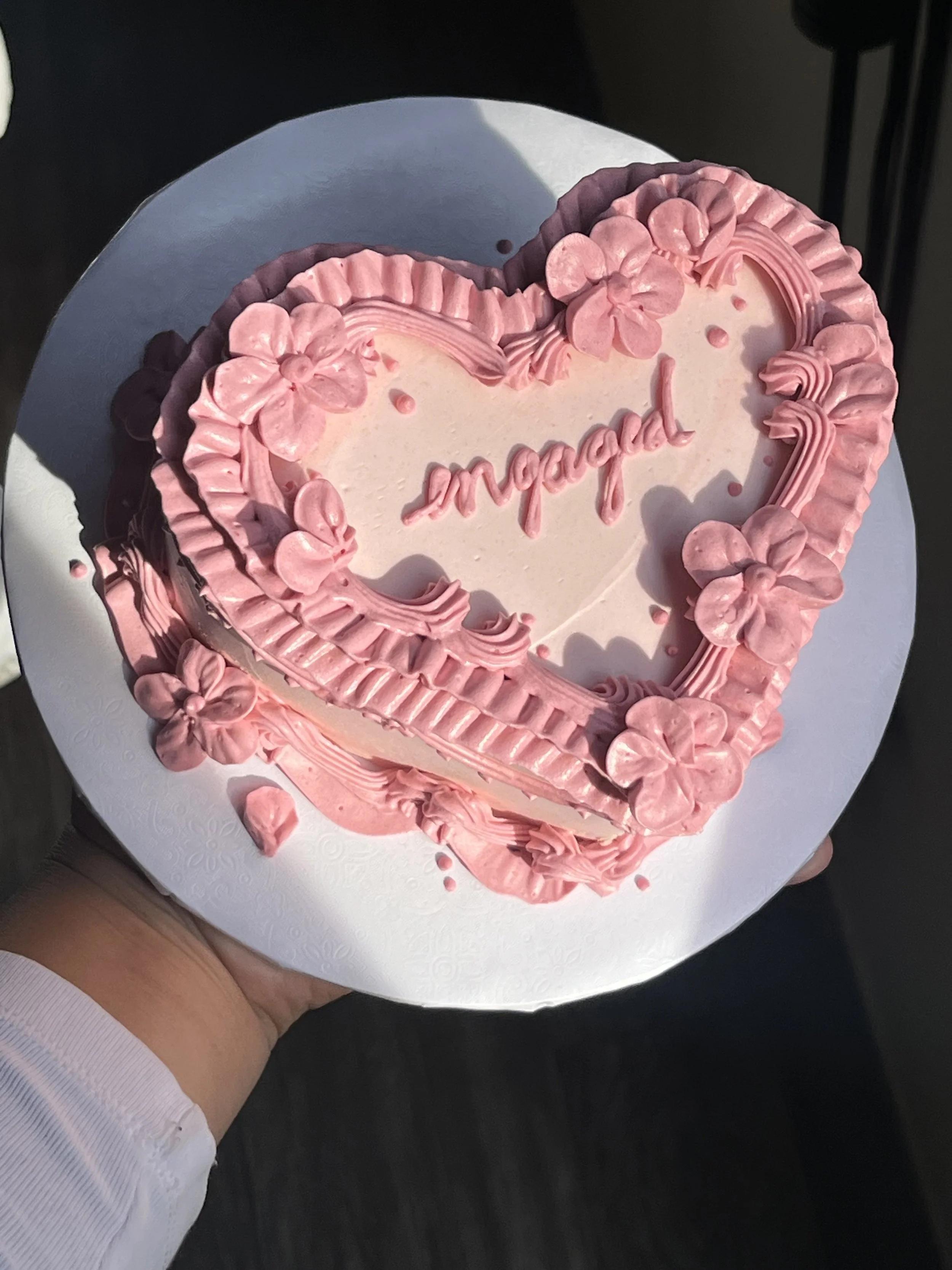 A pink, heart-shaped cake with decorative frosting flowers and the word 'married' written in pink icing.