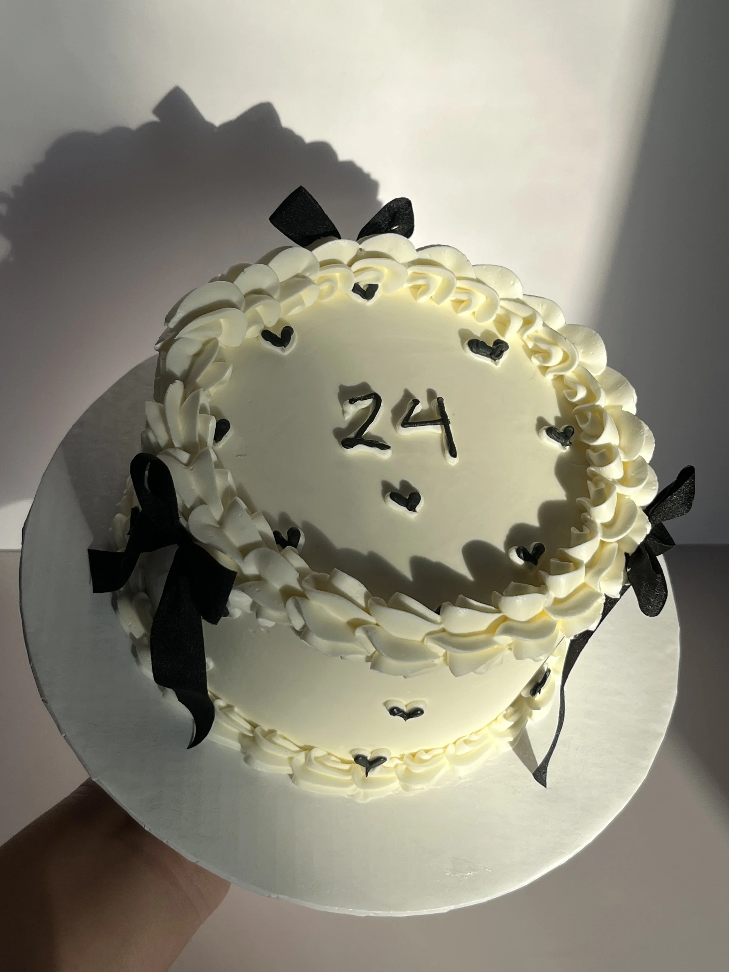 A white cake decorated with white icing and black ribbons, with the number 24 written in black on top.