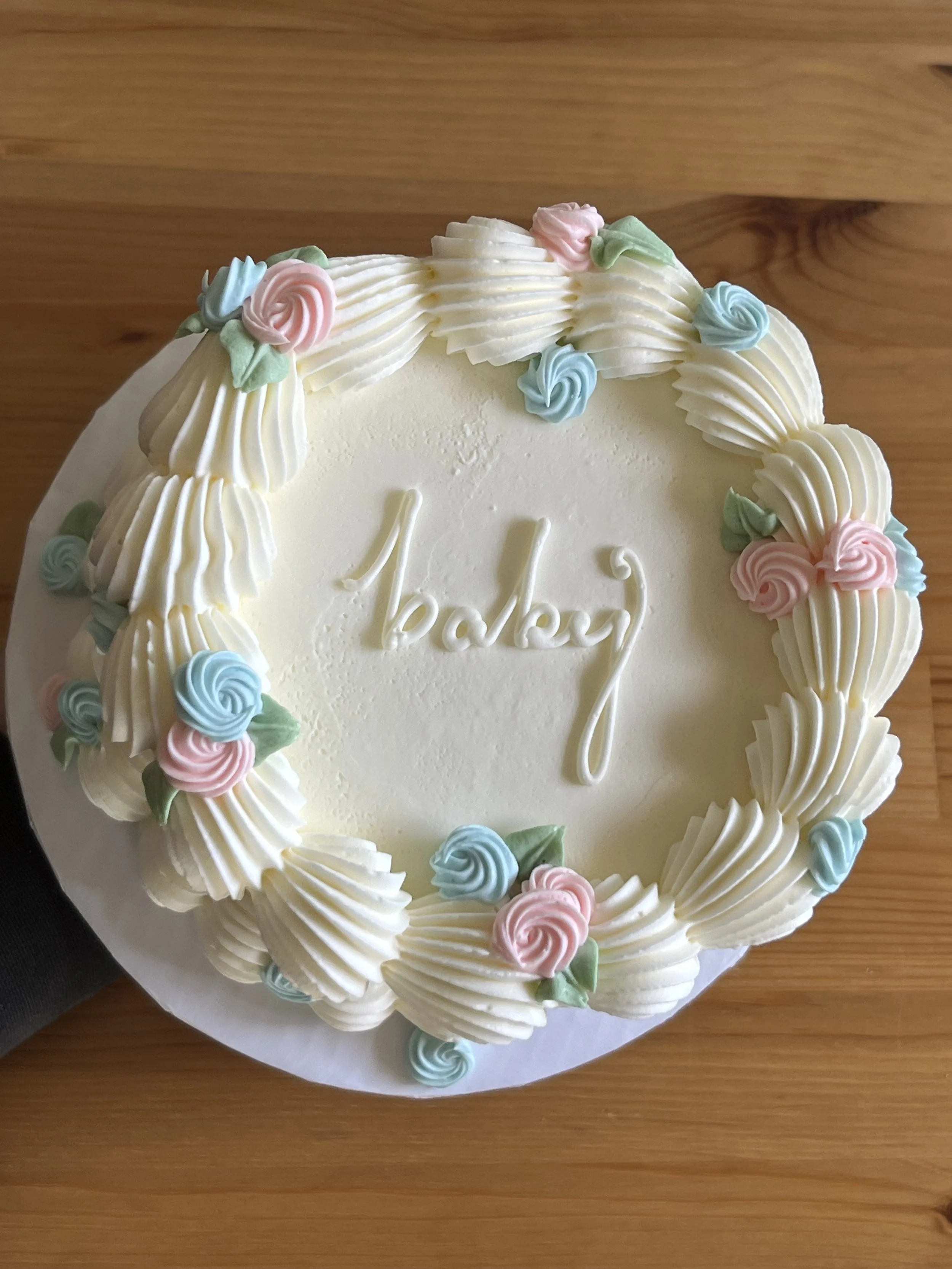 A round white birthday cake decorated with pastel-colored buttercream roses and piped swirls, with the partial word 'birthday' visible in the center.