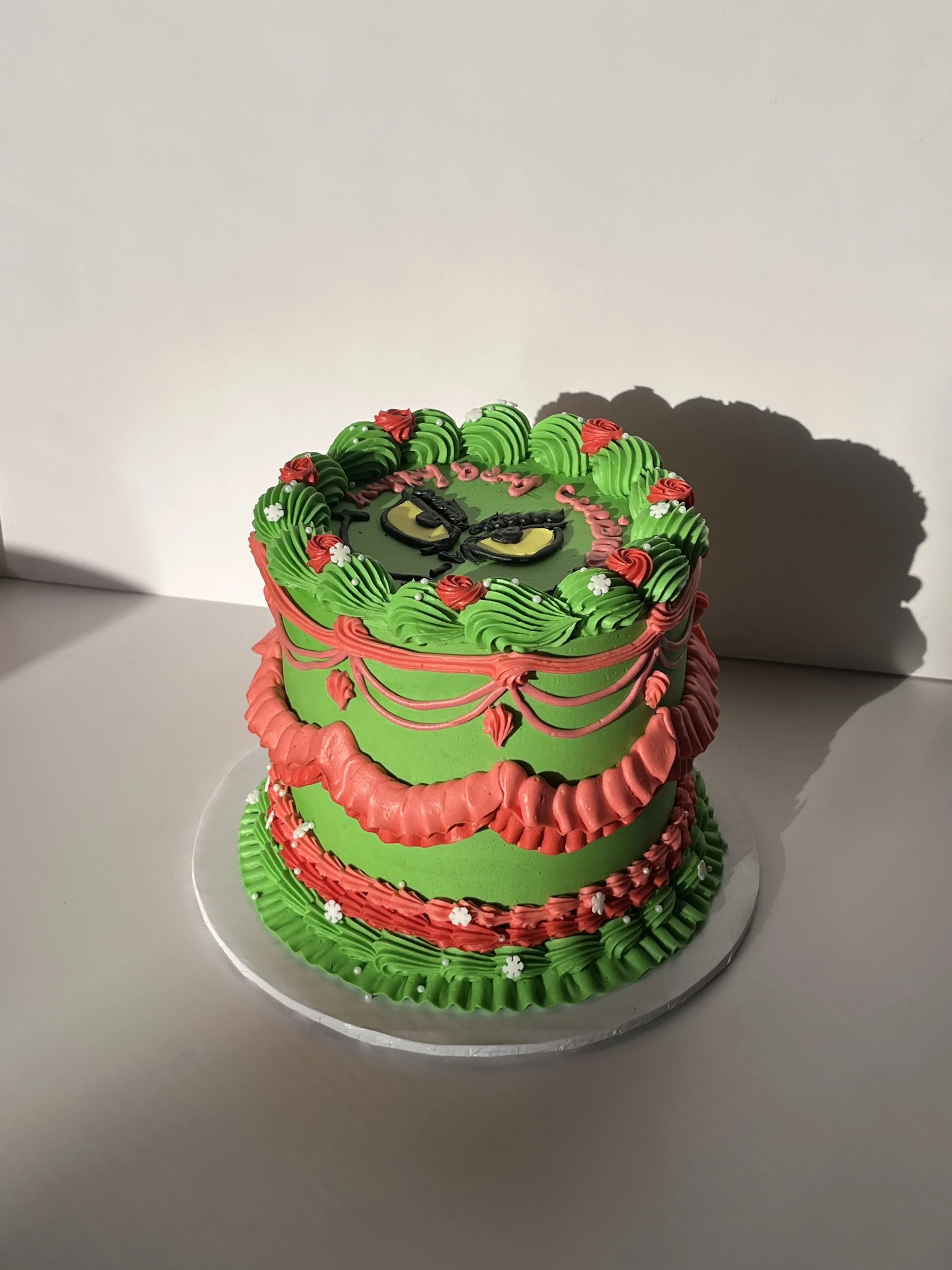 Colorful birthday cake decorated with green, red, and white icing, featuring a cartoon face and the words 'Happy Birthday' on top.