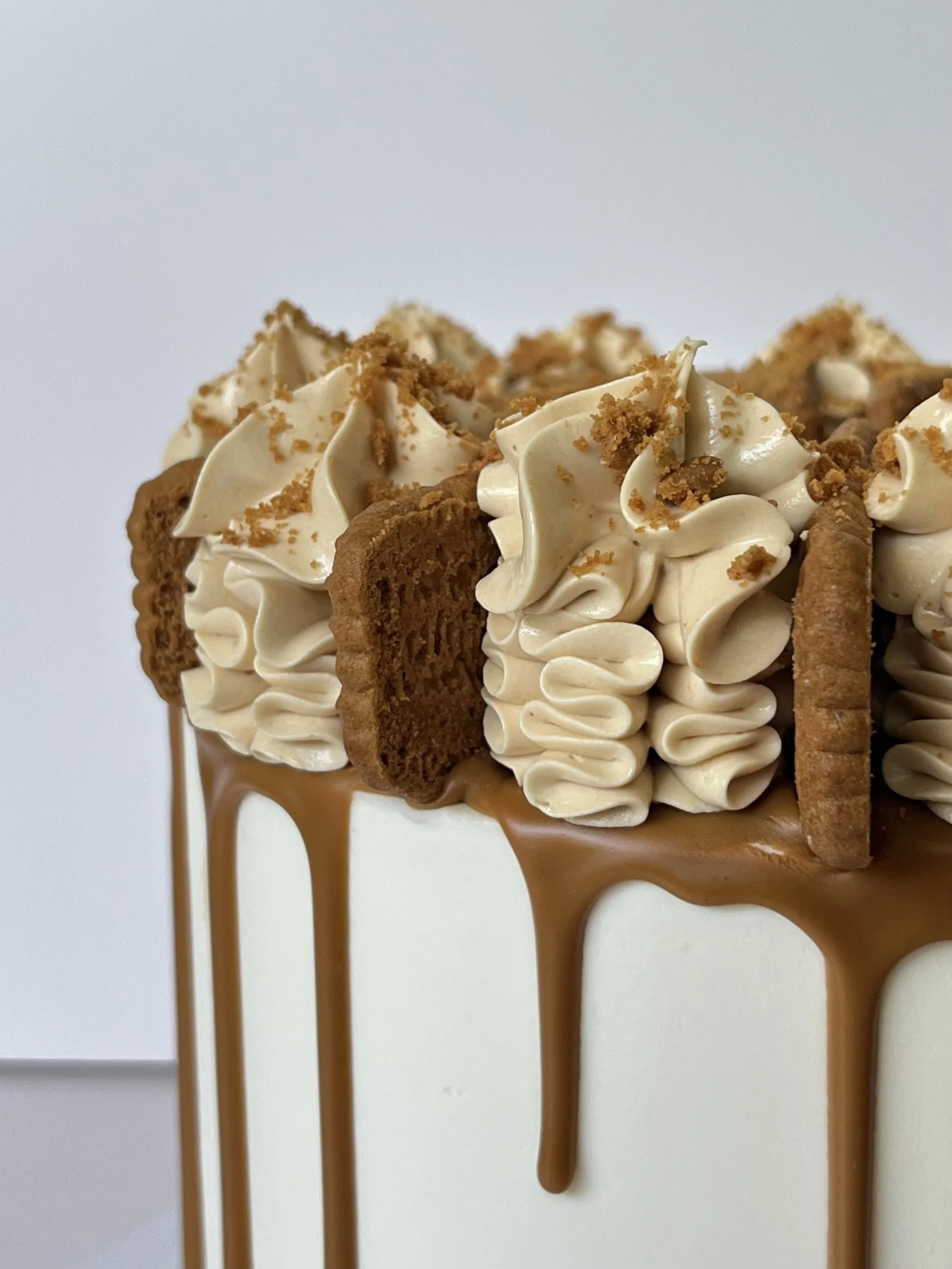 Close-up of a decorated dessert with cream, chocolate, cookies, and caramel drizzle on a white background.