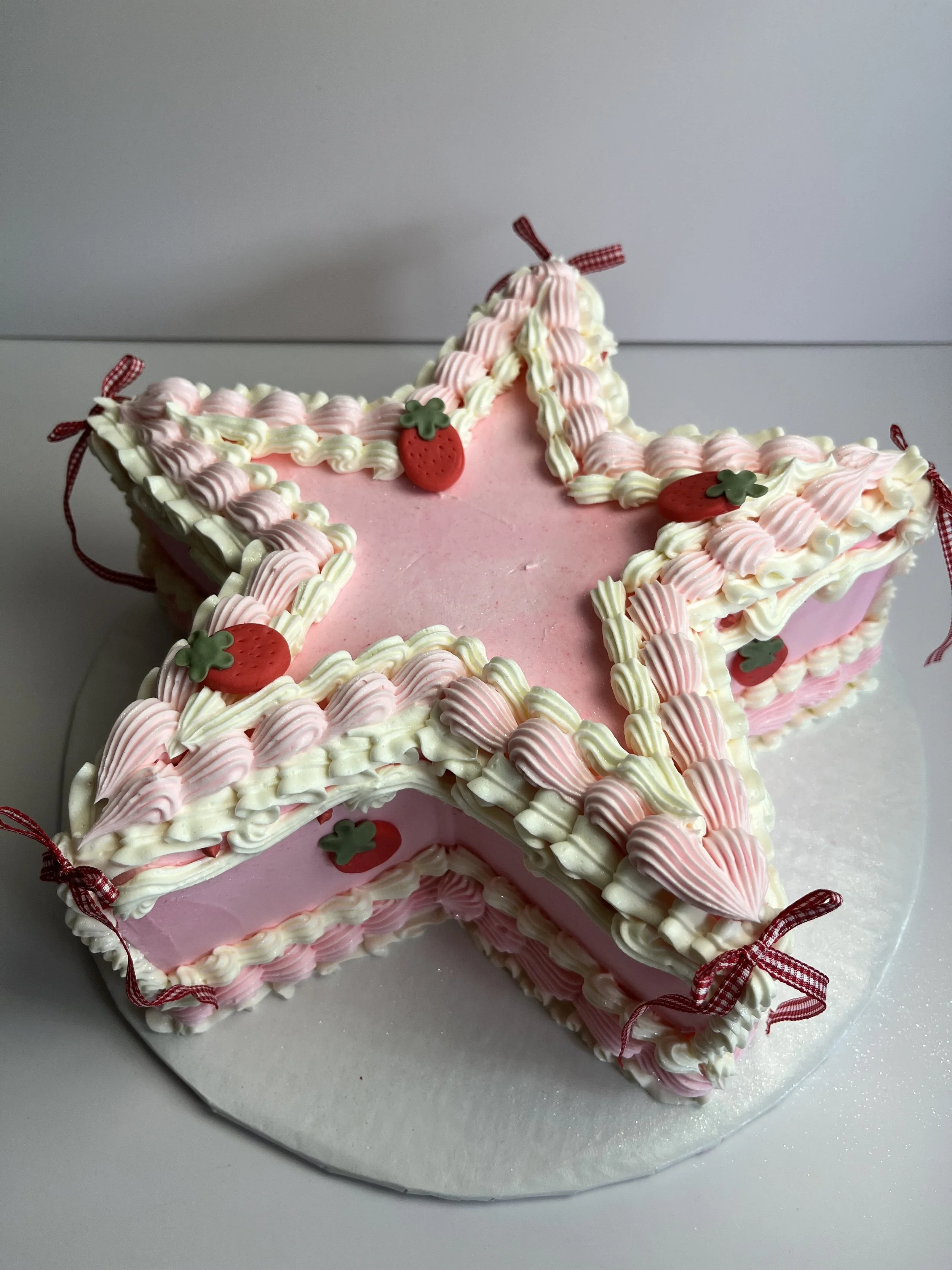 Decorative cake shaped like the number '1' with pink and white frosting, small strawberry and green leaf decorations, and tied with red ribbons.