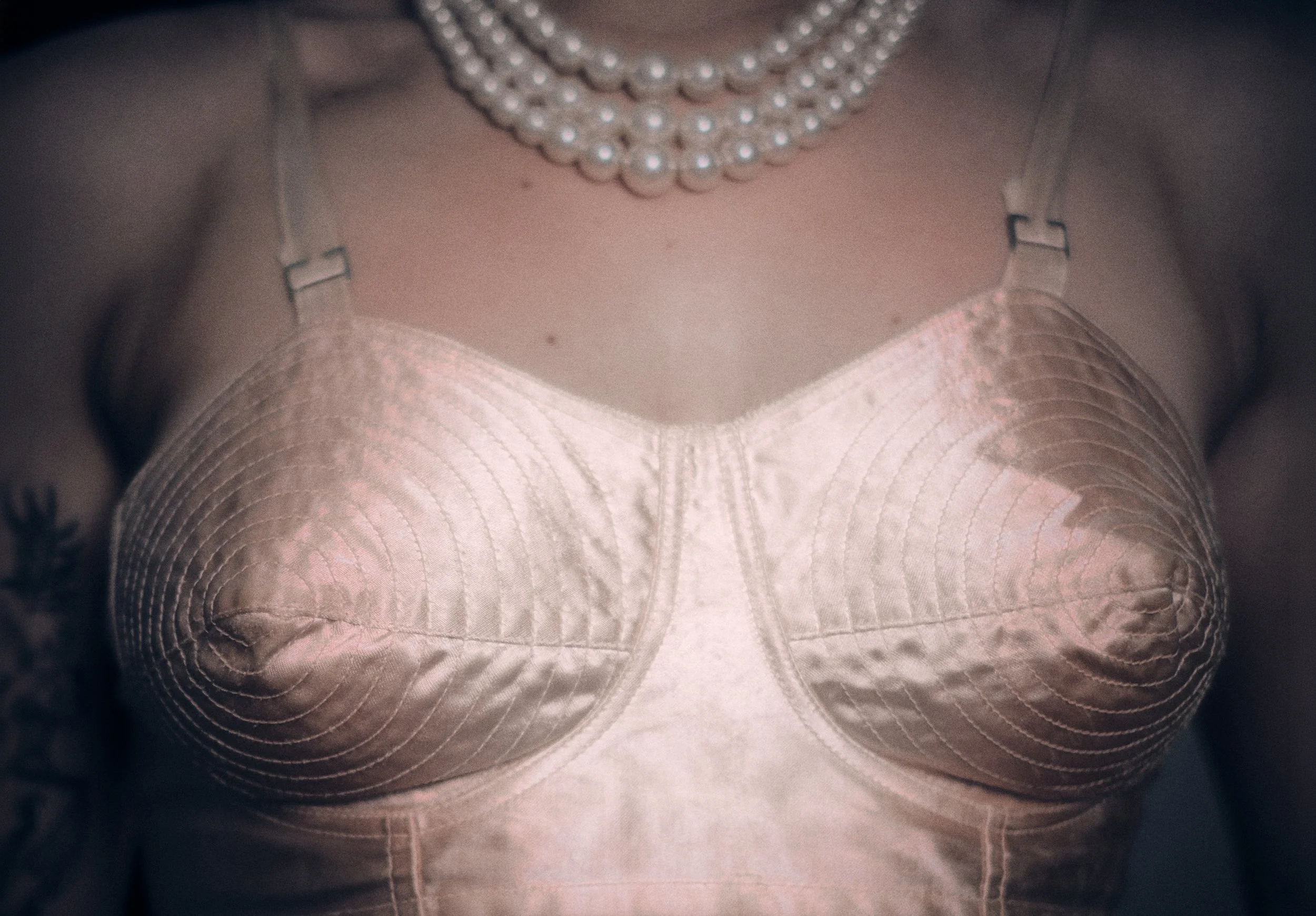 Close-up of a person wearing a white beaded necklace, mesh top, and decorative harness straps.