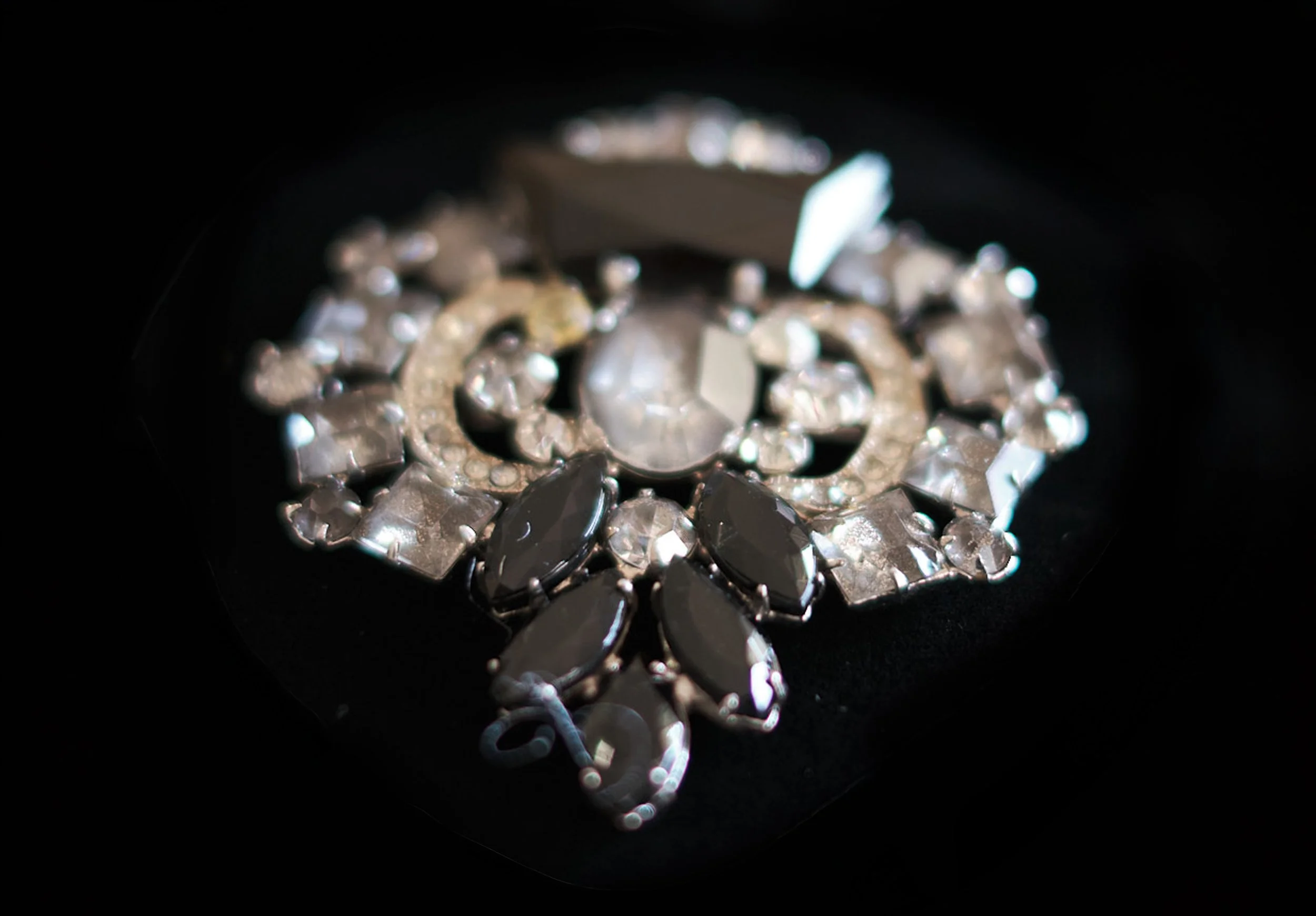 Close-up of an ornate vintage brooch featuring faceted dark gemstones and metallic embellishments on black fabric