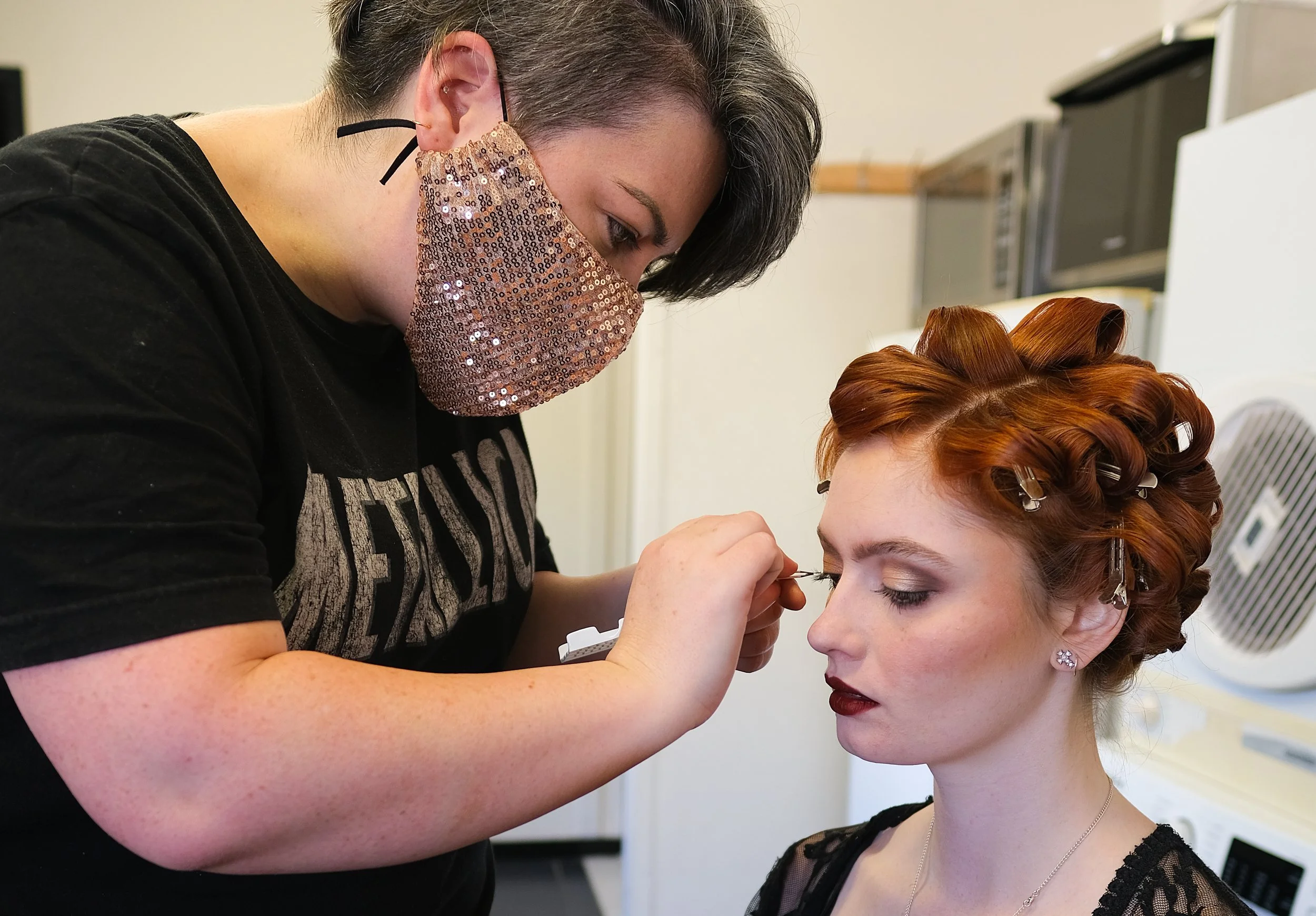 Makeup artist applying eyeliner to a red-haired woman with pinned-up hair
