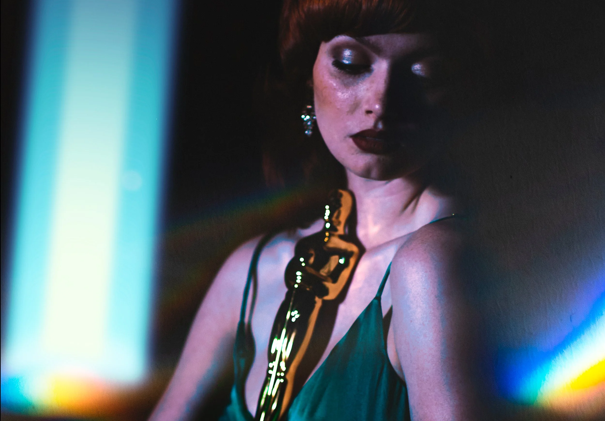 Close-up of a woman in a teal dress and ornate jewelry under dramatic blue and purple lighting