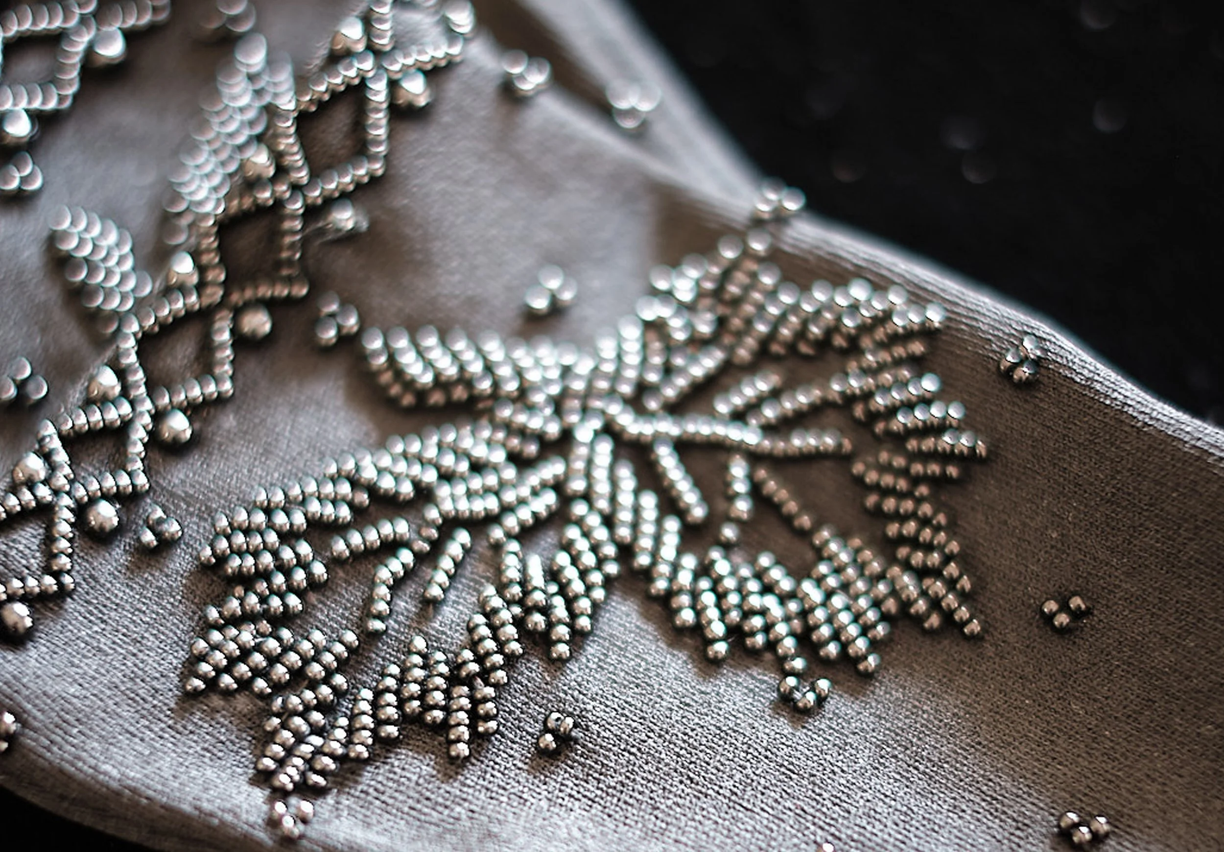Close-up of silver beaded jewelry arranged on dark textured fabric