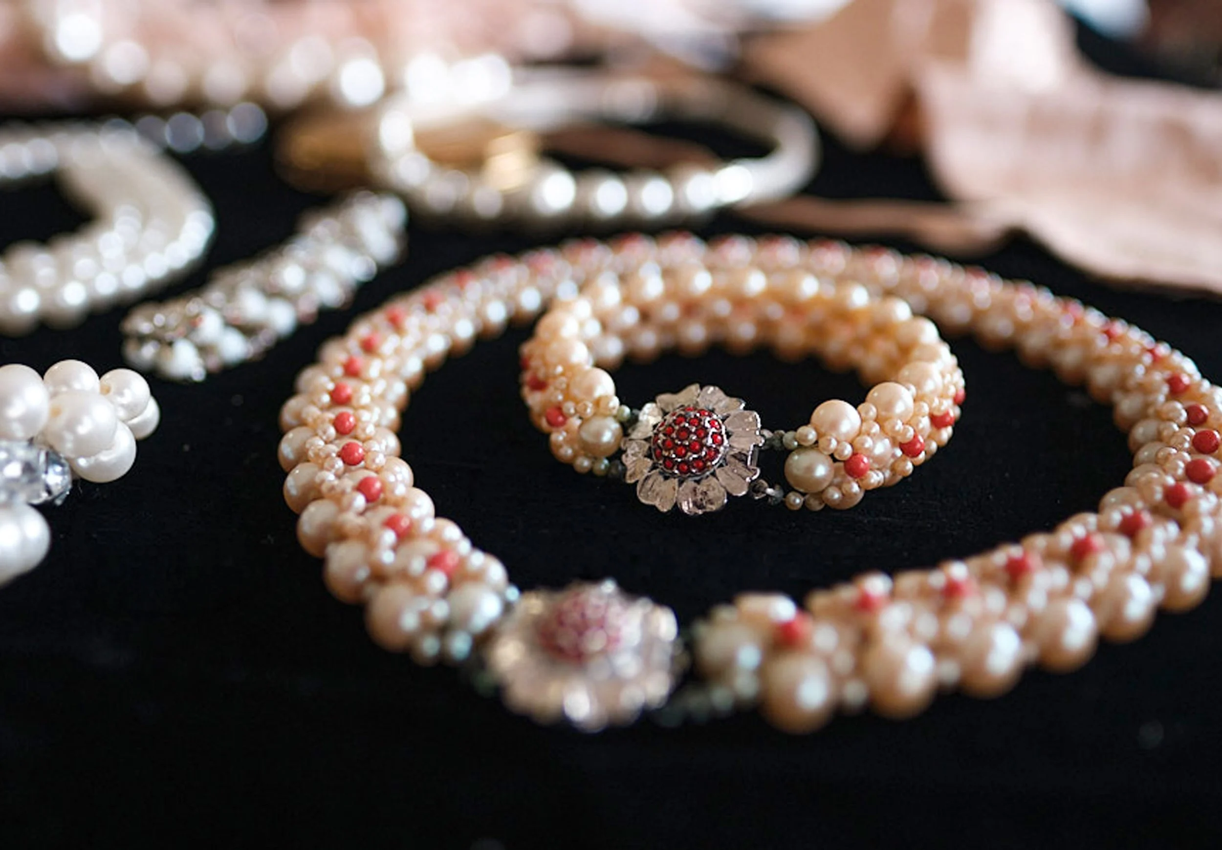Close-up of vintage pearl and coral beaded jewelry with a floral clasp on black fabric