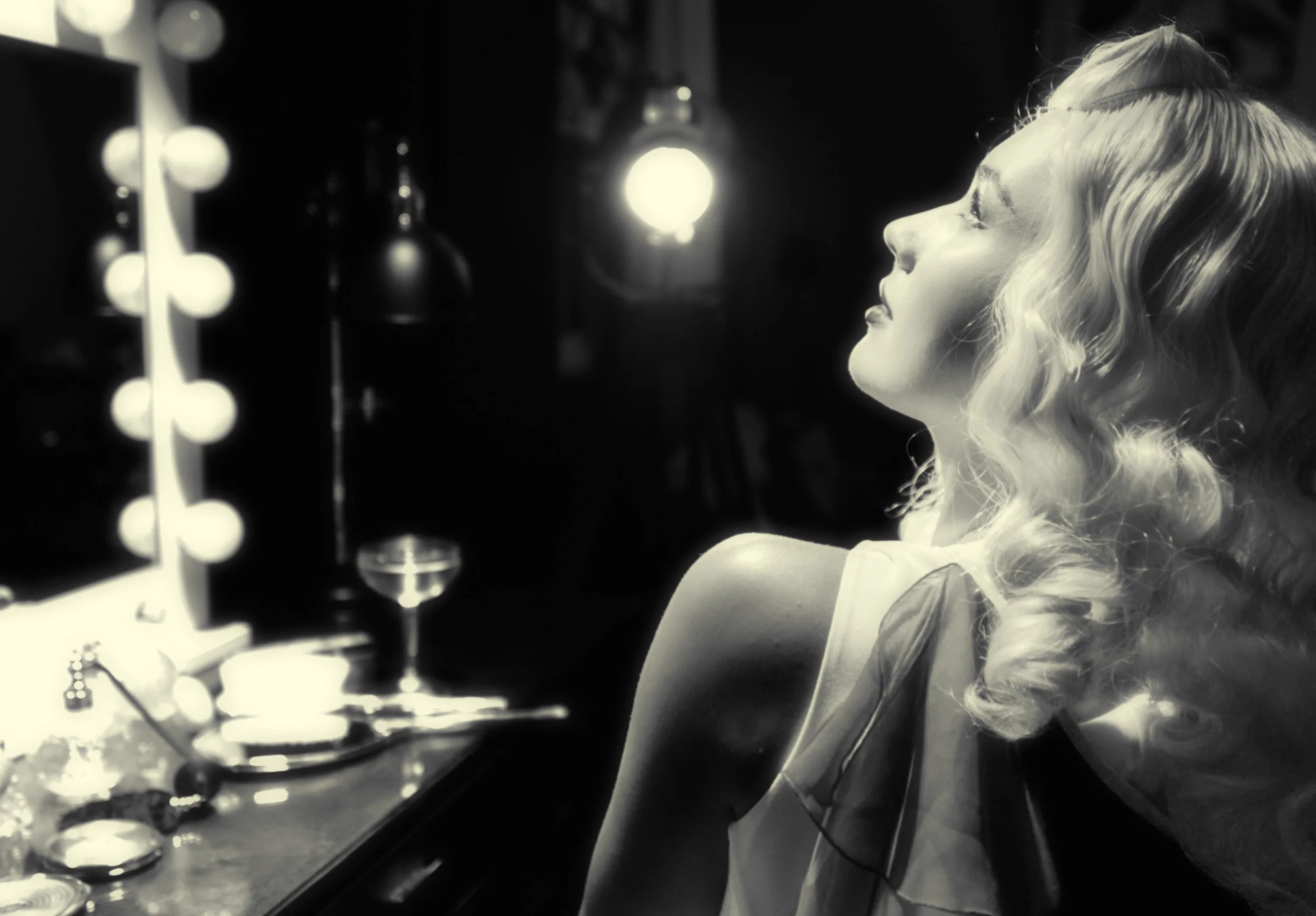Black-and-white photo of a woman singing or speaking in profile beside a microphone and illuminated studio lights.