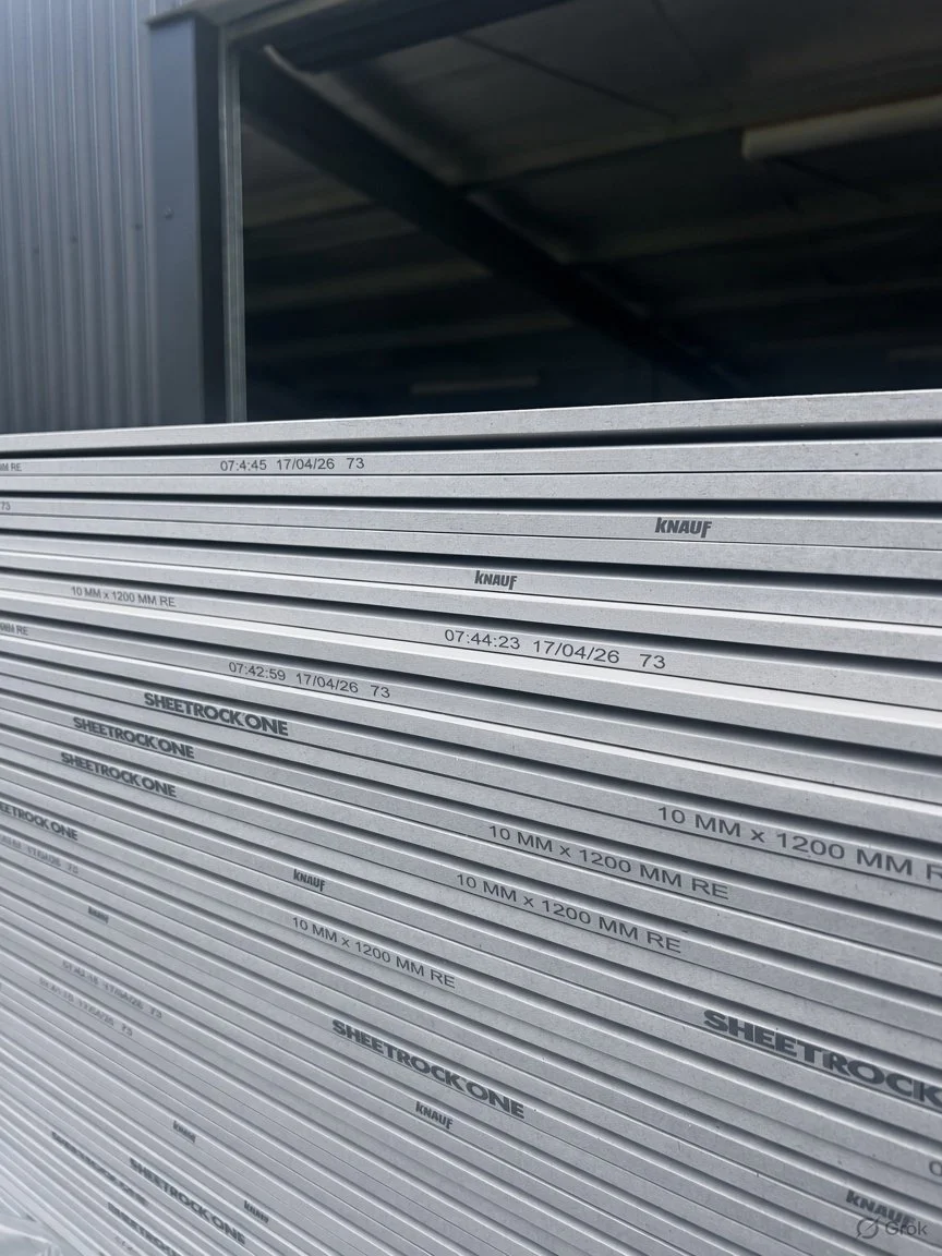 Stack of sheetrock panels labeled with specifications, stored in a warehouse.