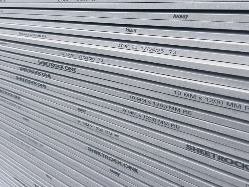 Stacks of grey drywall sheets labeled with technical specifications including '10 mm x 1200 mm RE' and 'SHEETROCK ONE' along with branding from 'KNAUF'.