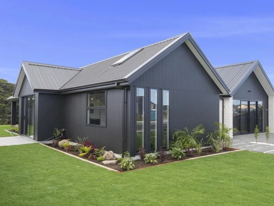 Modern house with gray metal siding and a sloped roof, surrounded by a well-maintained lawn and small landscaped garden.