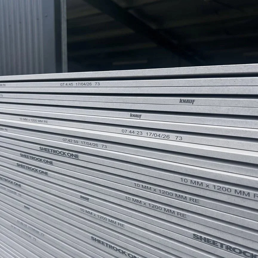 Stacks of metal sheets labeled with specifications including size, date, and brand, stored outdoors under a metal roof.