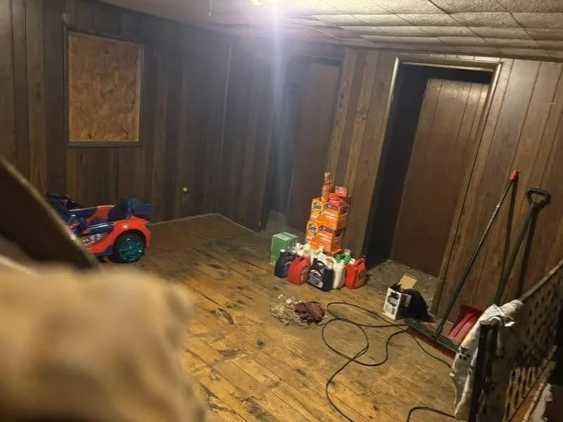 An empty room with wooden walls and floor, containing gardening tools, a toy car, and stacks of bags of soil or mulch.