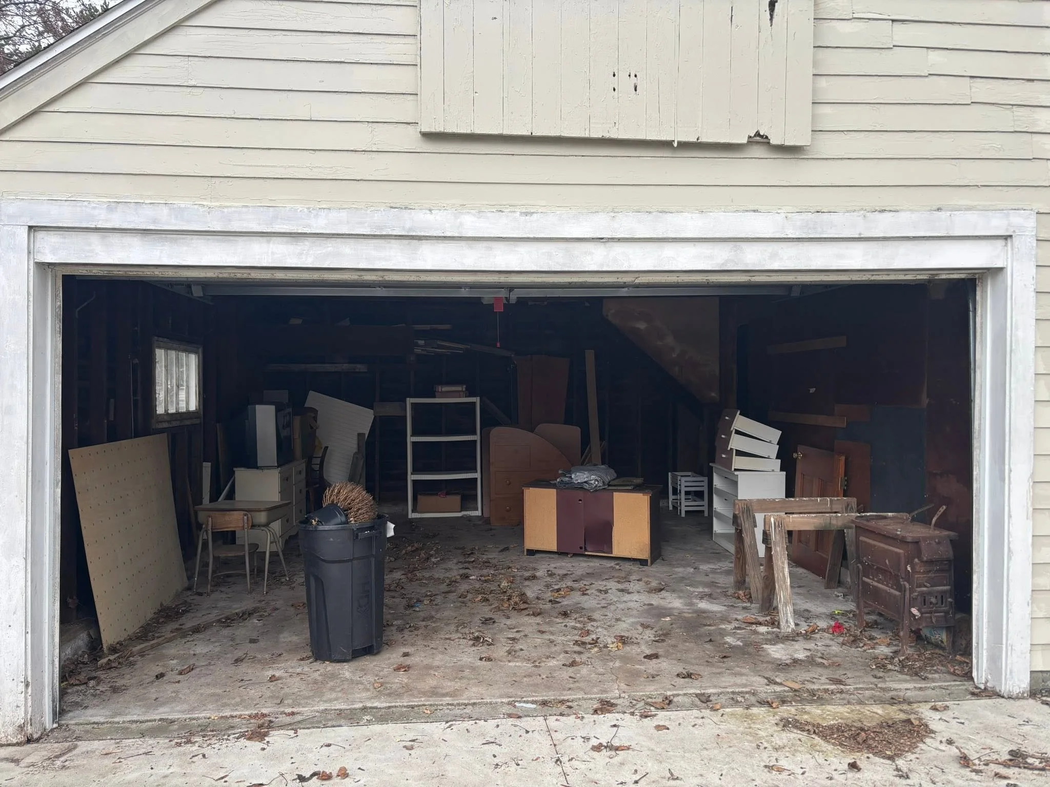 A cluttered garage with various pieces of furniture and items stored inside, viewed from the open garage door.