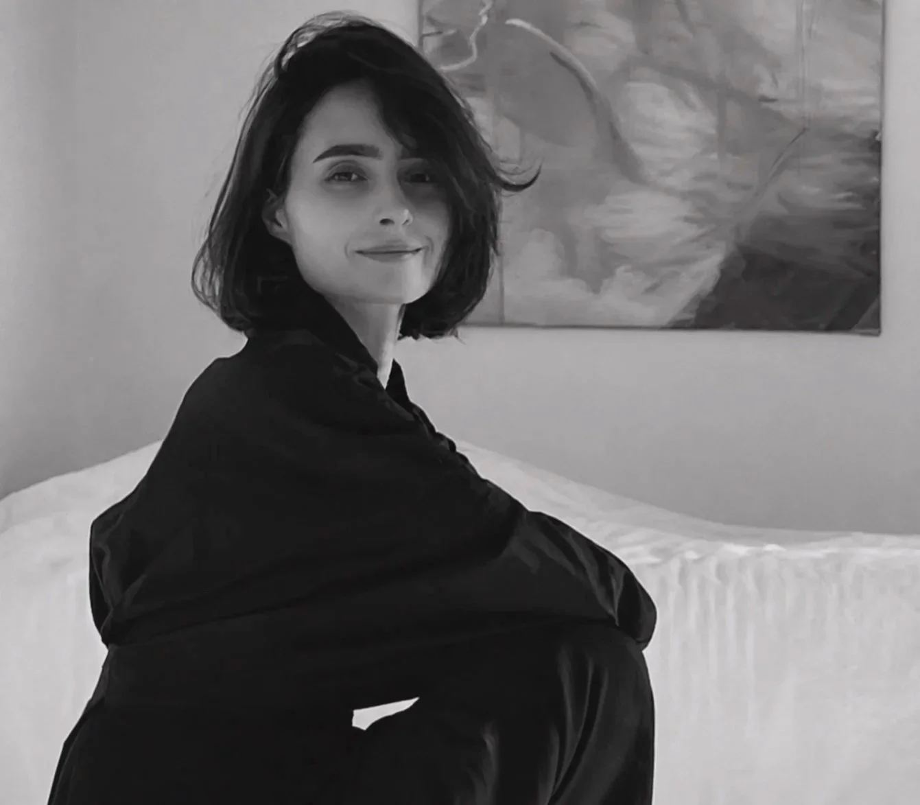 Black and white portrait of a seated woman, with an abstract painting in the background.