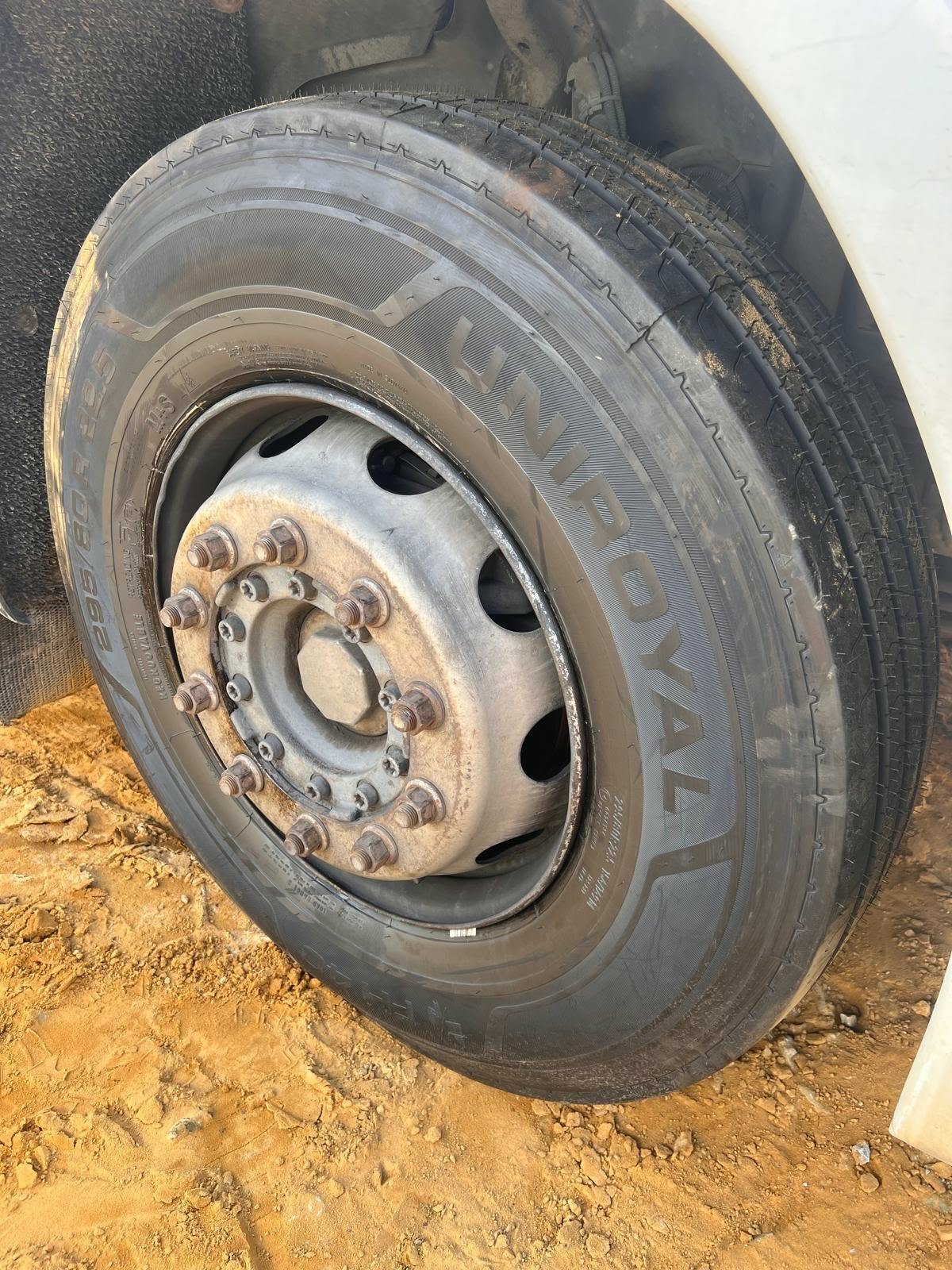 Close-up of a vehicle tire and wheel, with visible lug nuts, on a dirt surface.