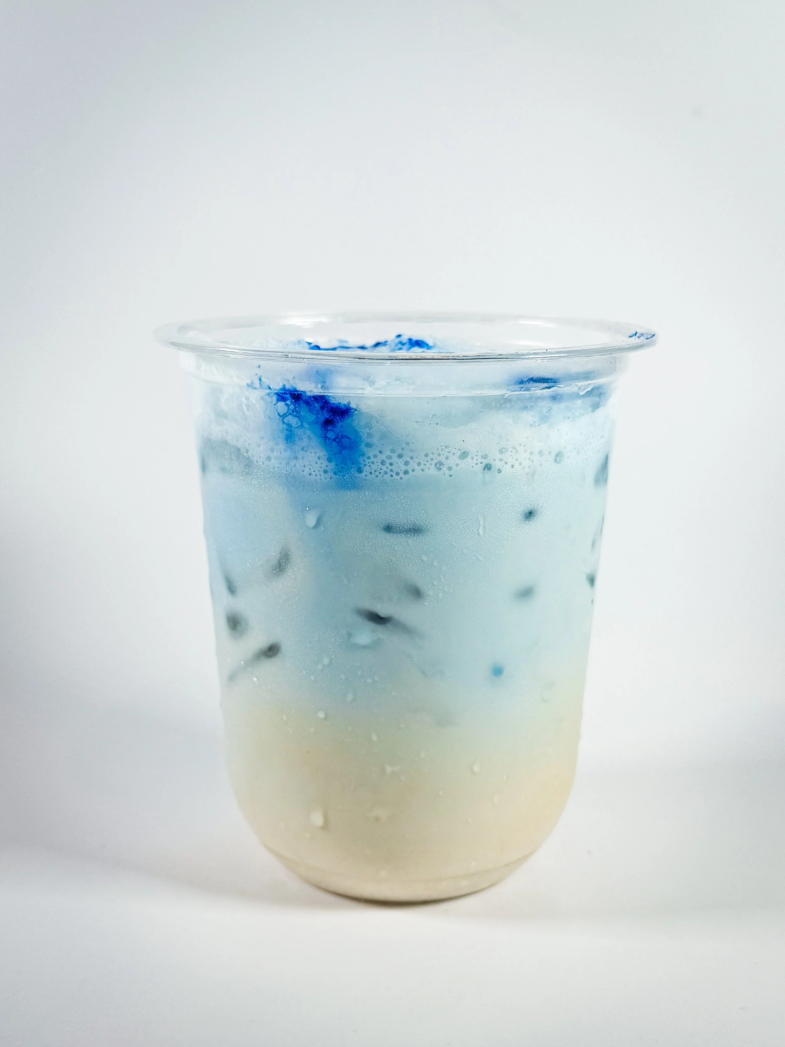 A clear plastic cup filled with a layered mixture of white and blue liquids with visible bubbles and swirling colors.