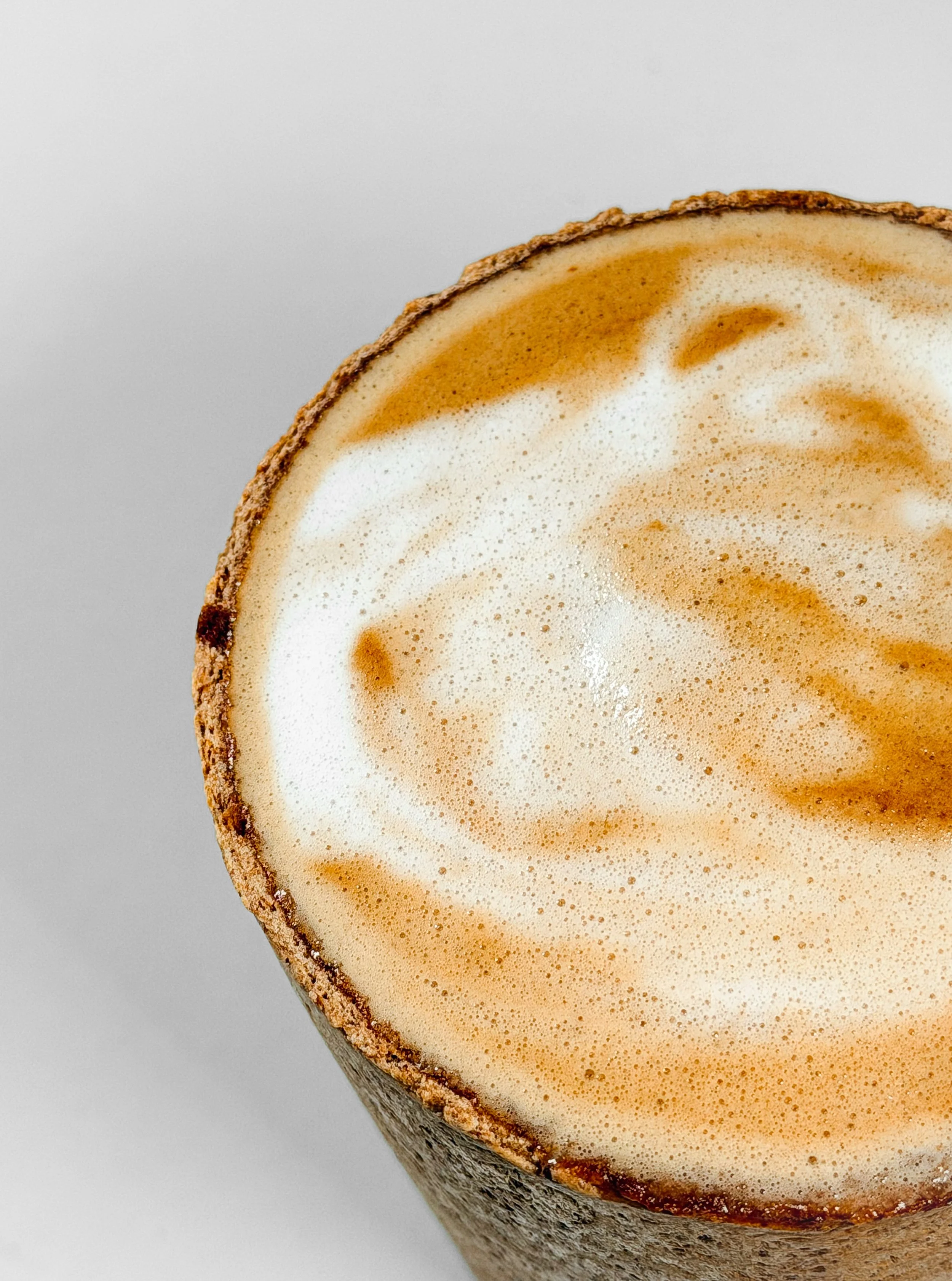 A close-up of a latte in a clear glass cup with foam and swirls, placed on a gray surface.