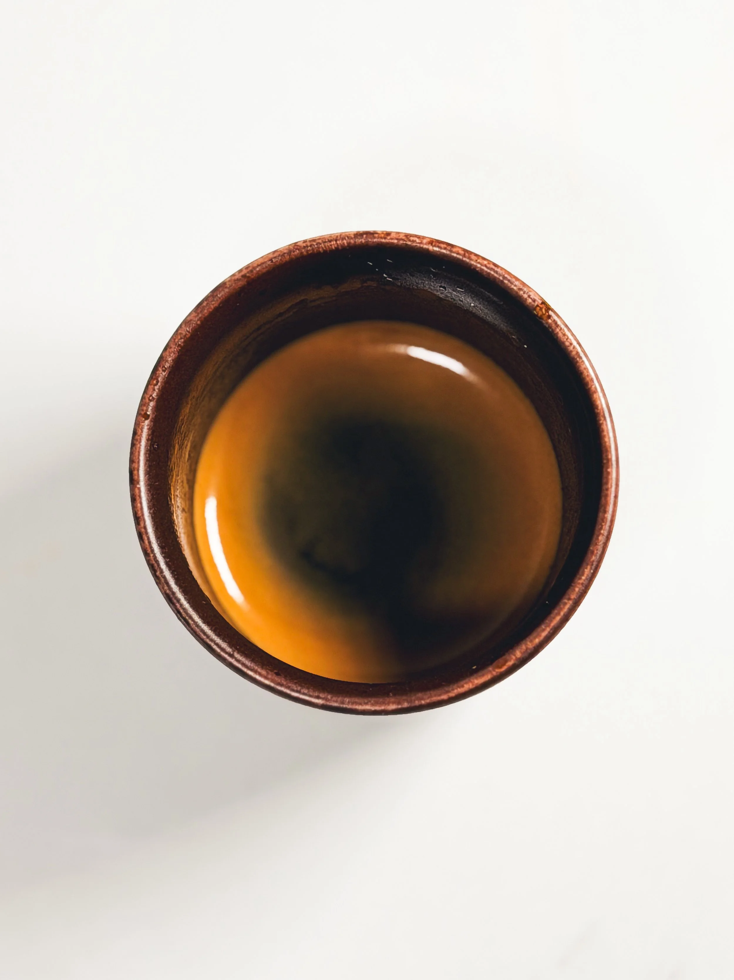 Top view of a brown ceramic cup filled with coffee on a white surface.