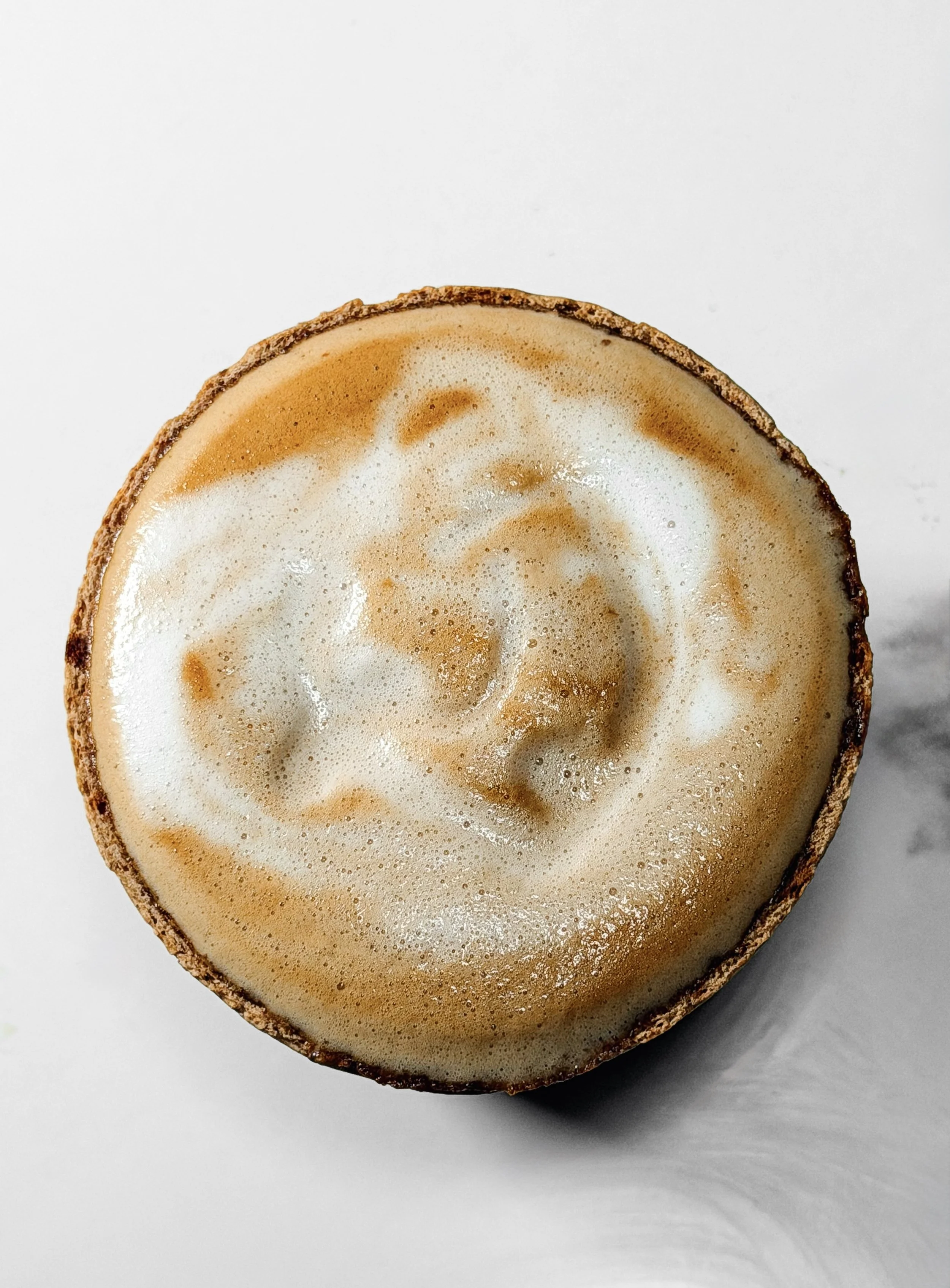 Close-up of a halved latte with foam and caramel swirls on a white surface.