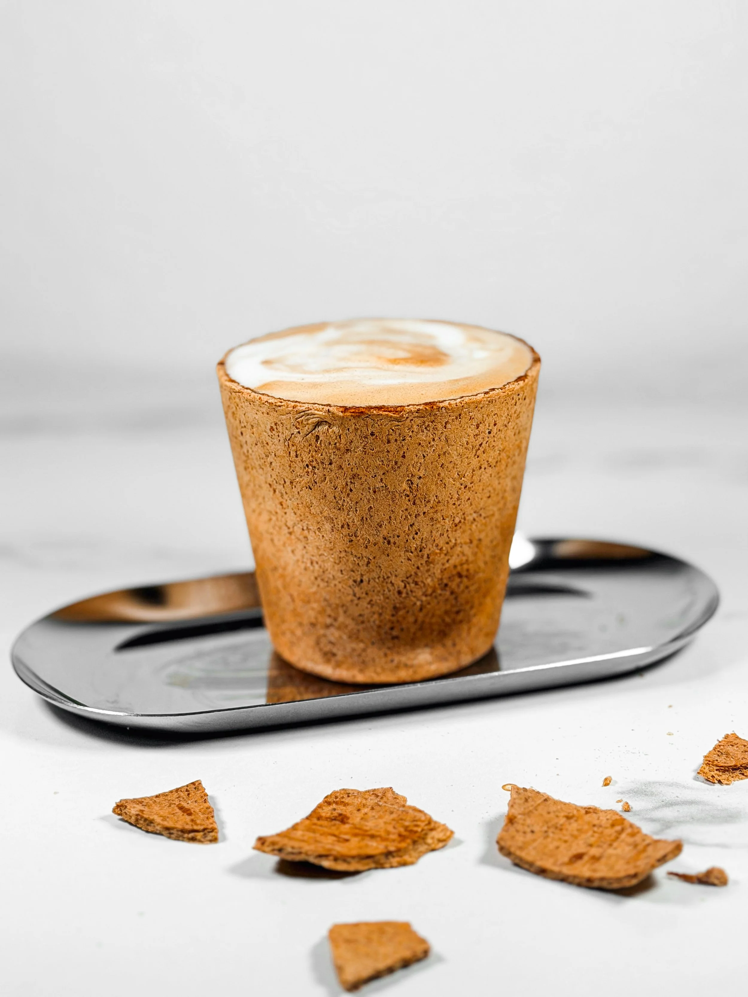 A partially broken egg in a toasted sandwich bread cone on a silver tray with broken pieces of bread on a white surface.