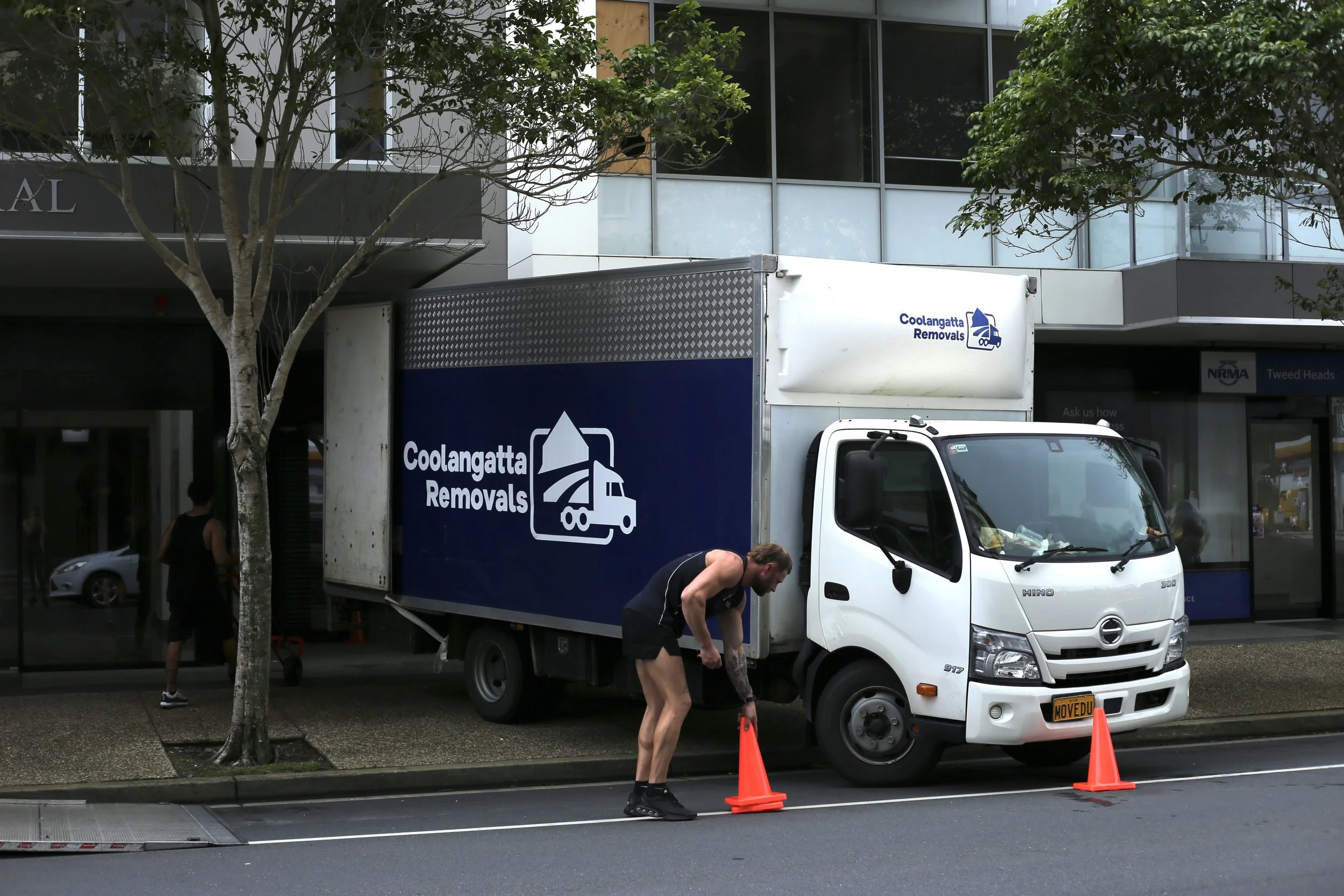 Coolangatta Removals moving truck parked outside a building with a worker placing orange traffic cones