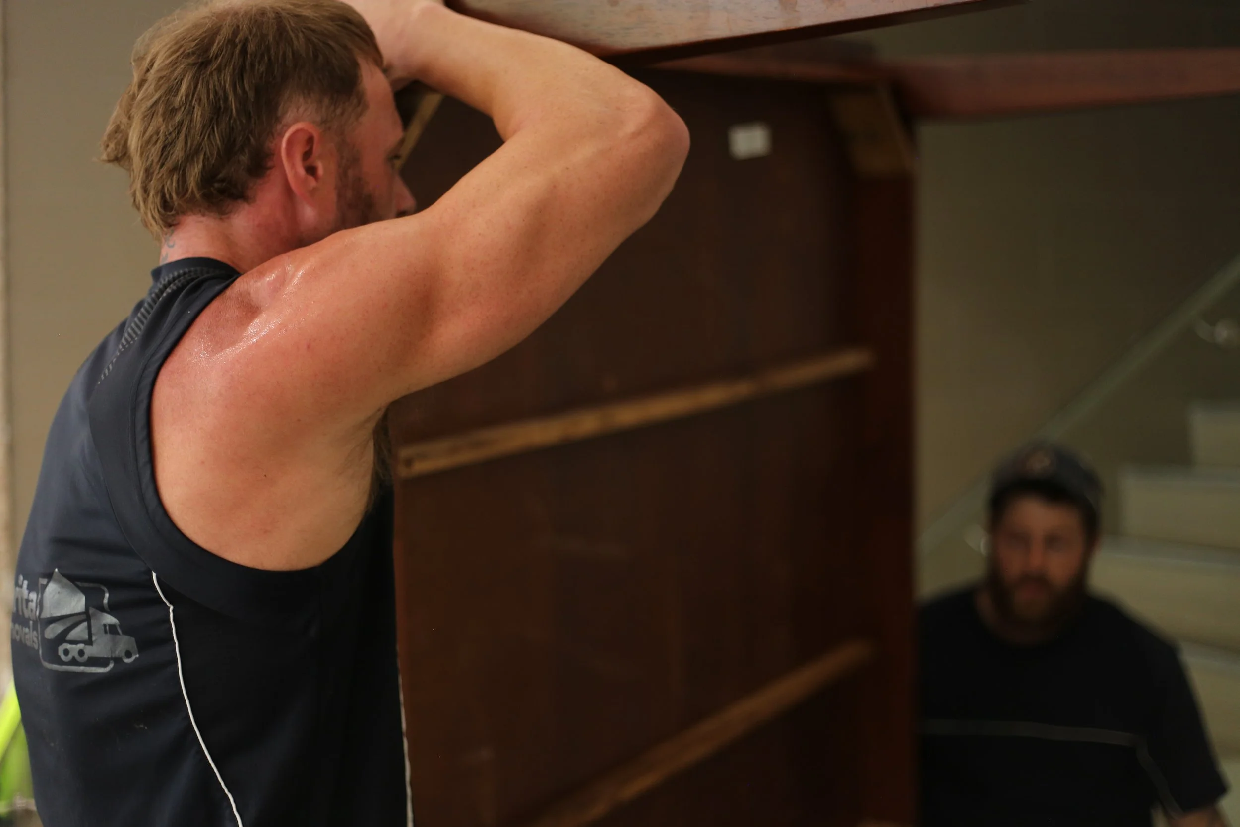 Man in a black shirt lifting or moving a large upright piano indoors