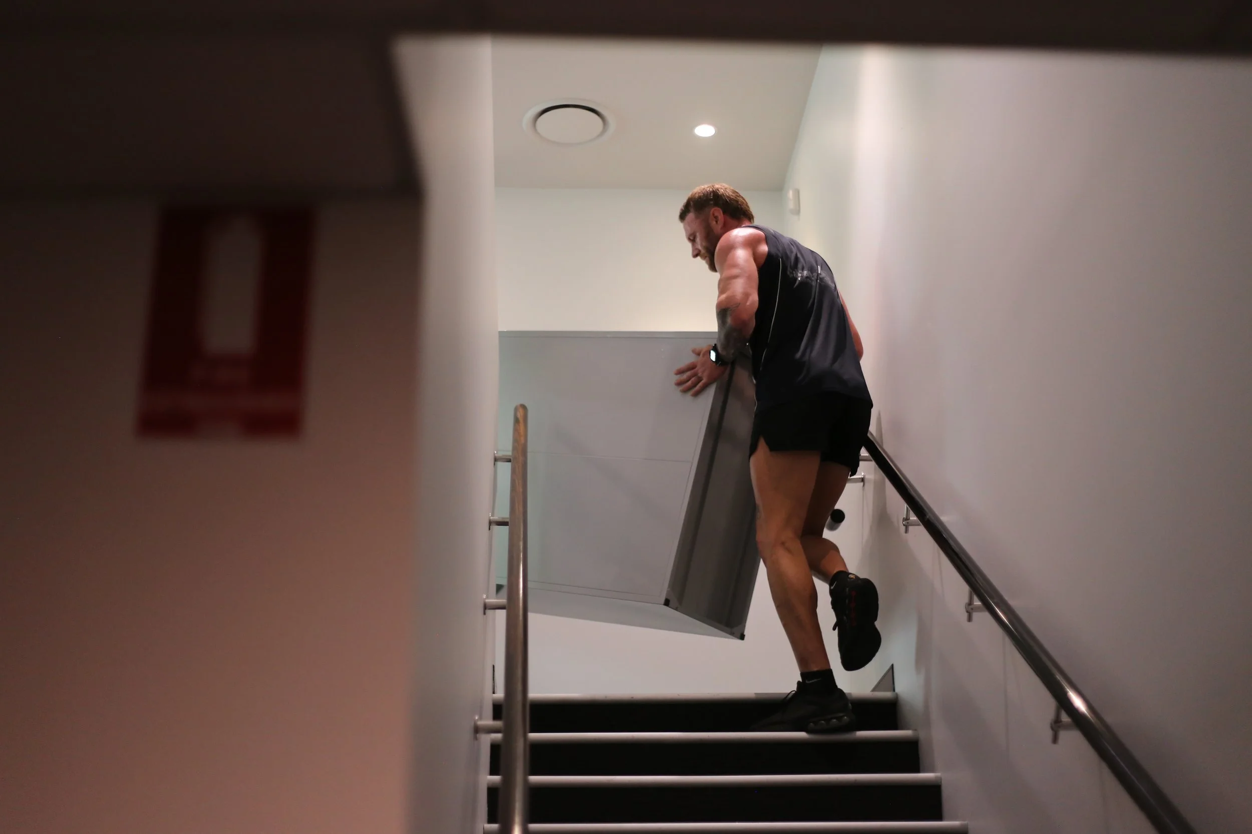 Muscular man in athletic clothing climbing stairs indoors while holding the handrail.
