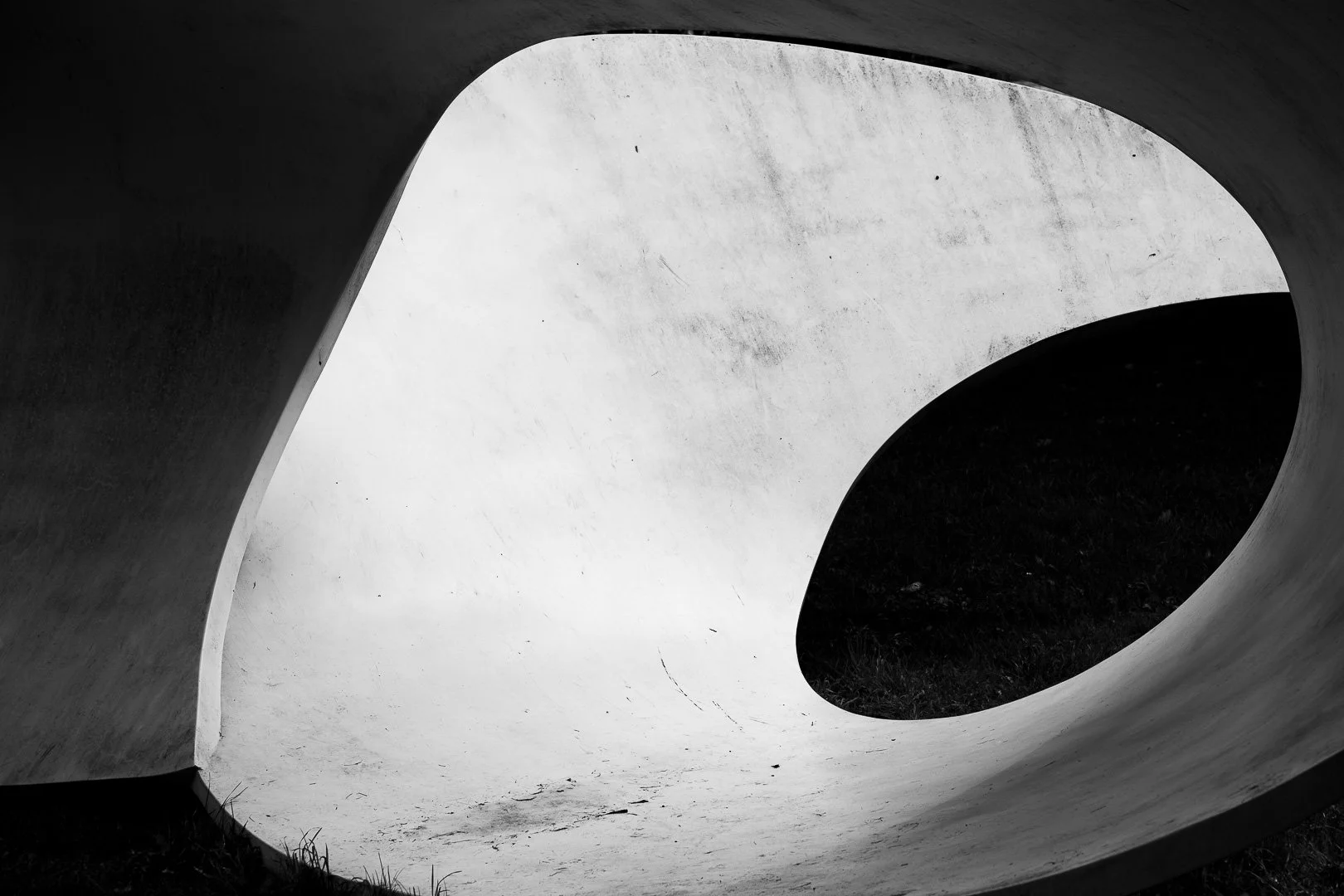 Black and white photograph of a modern architectural structure with curved walls and an elliptical opening, overlooking a dark outdoor area.
