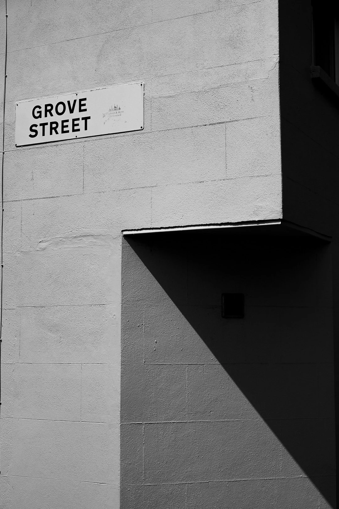 Black and white photo of a street sign reading 'Grove Street' attached to a building wall, with a strong shadow cast on the wall.